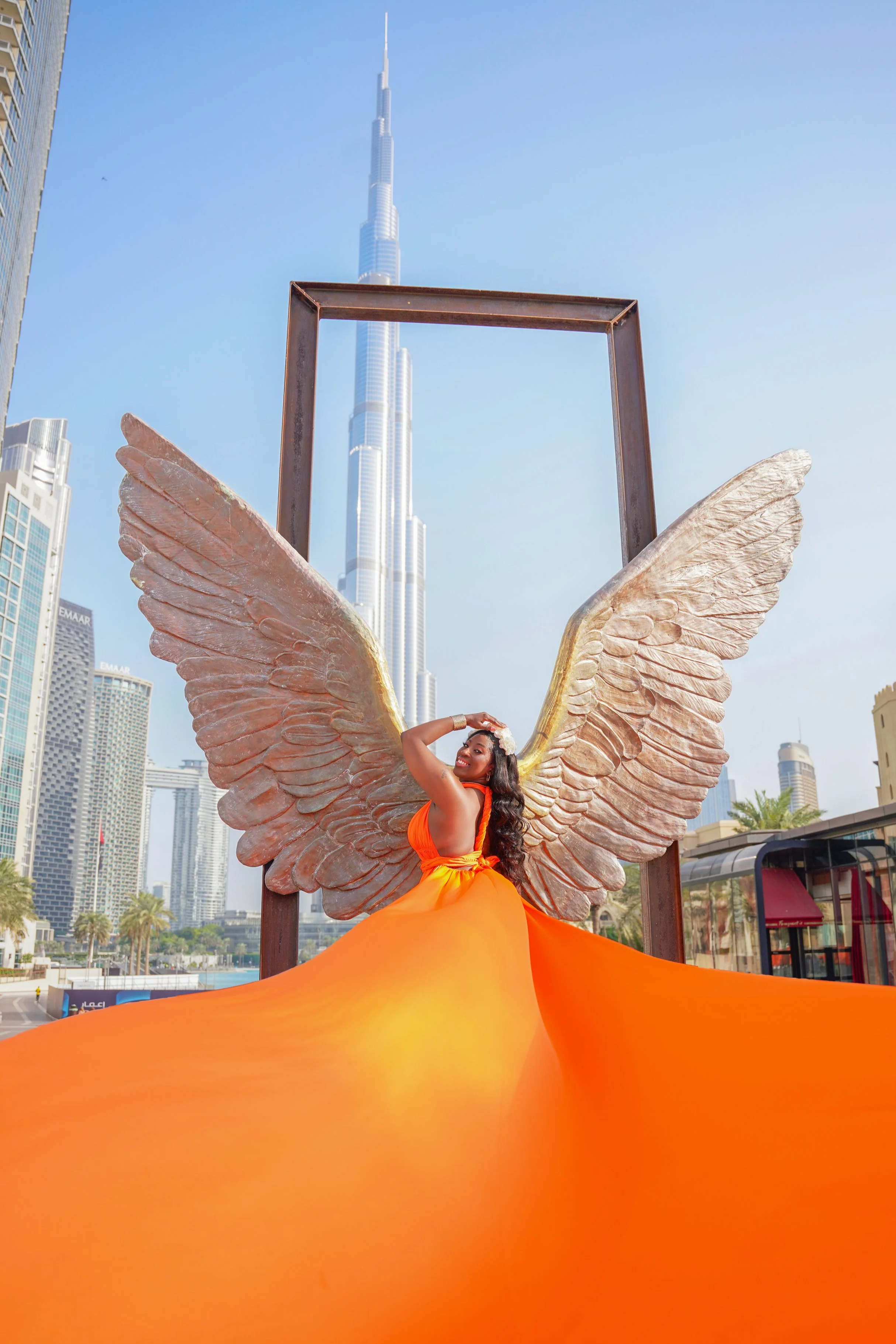 Shyla Bryant, founder of TryShy Travel, wearing a flowing orange dress in front of the Wings of Mexico sculpture in Dubai.