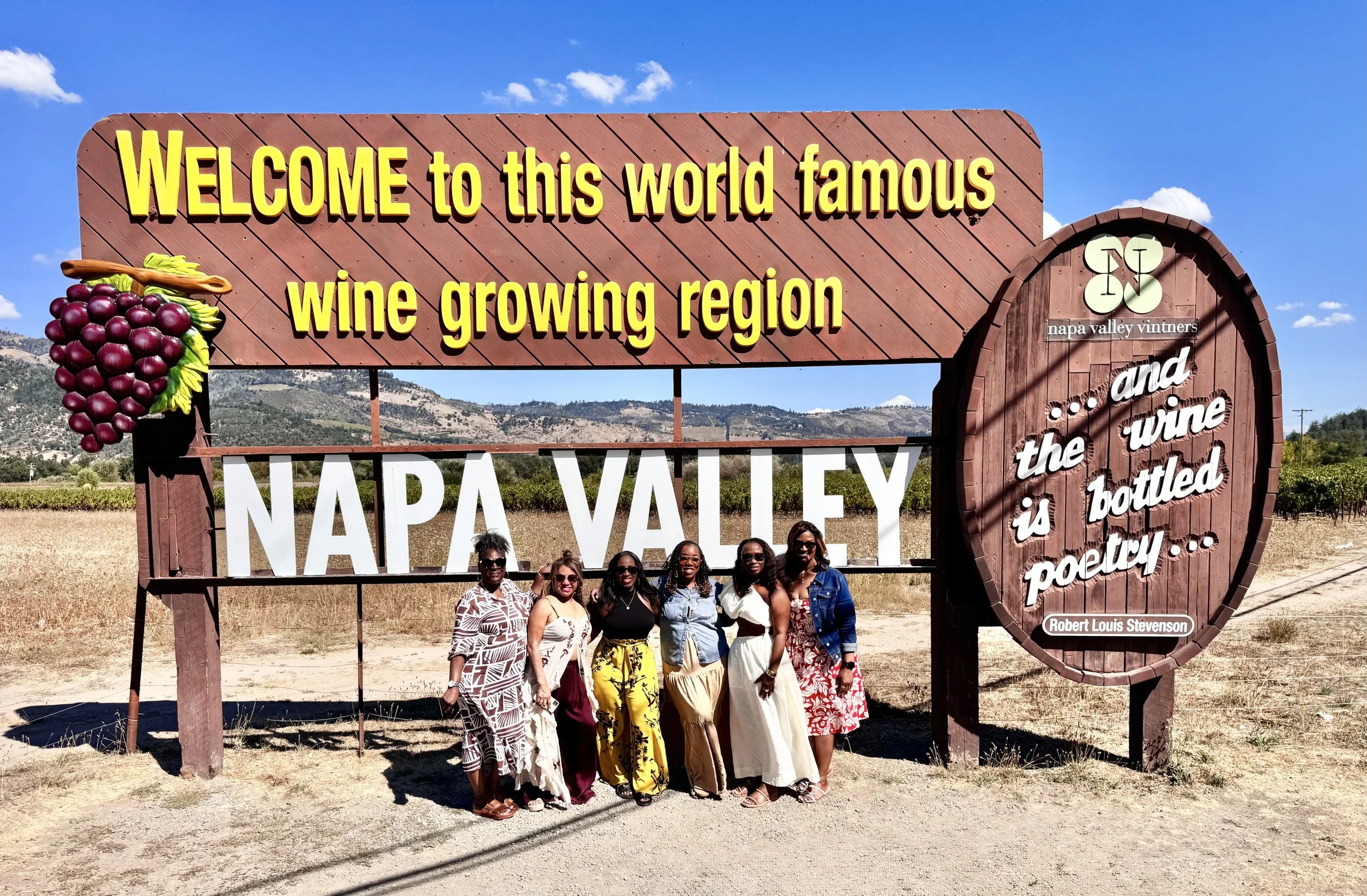 Six women from a TryShy Travel group trip posing beneath the iconic Welcome to Napa Valley sign in California.