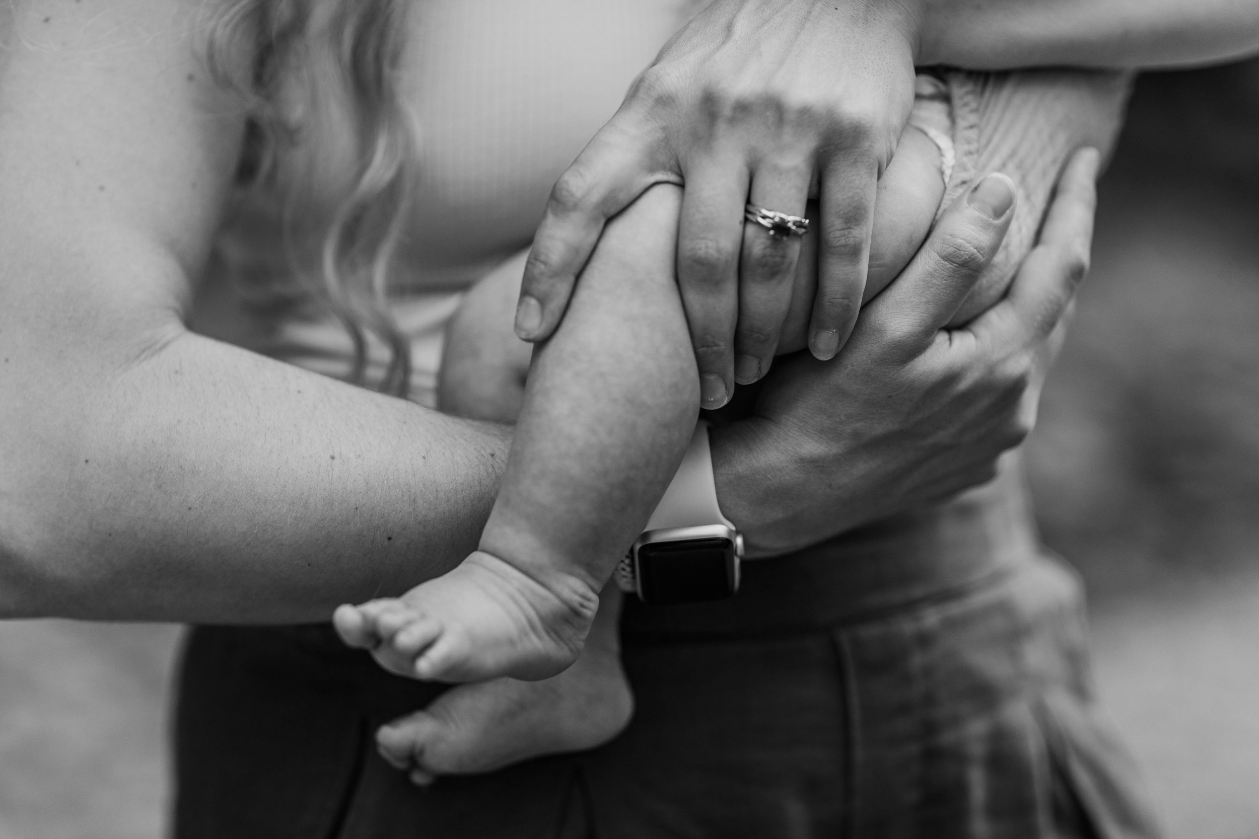 A close-up black and white photo of an adult hand holding a child's hand, with the adult wearing a wedding ring and a smartwatch.