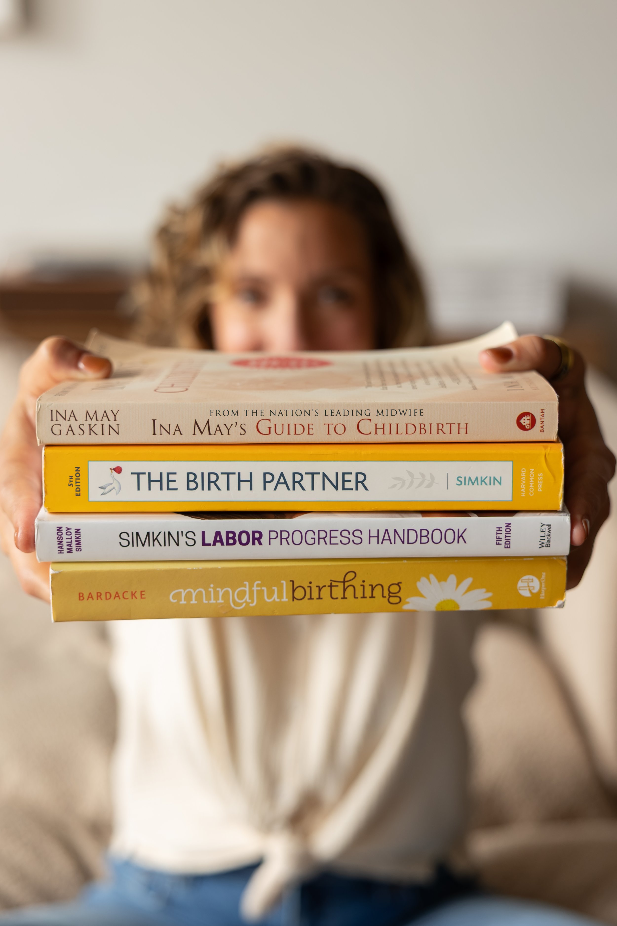 A person holding a stack of books about childbirth and pregnancy, with her face partially visible behind the books.