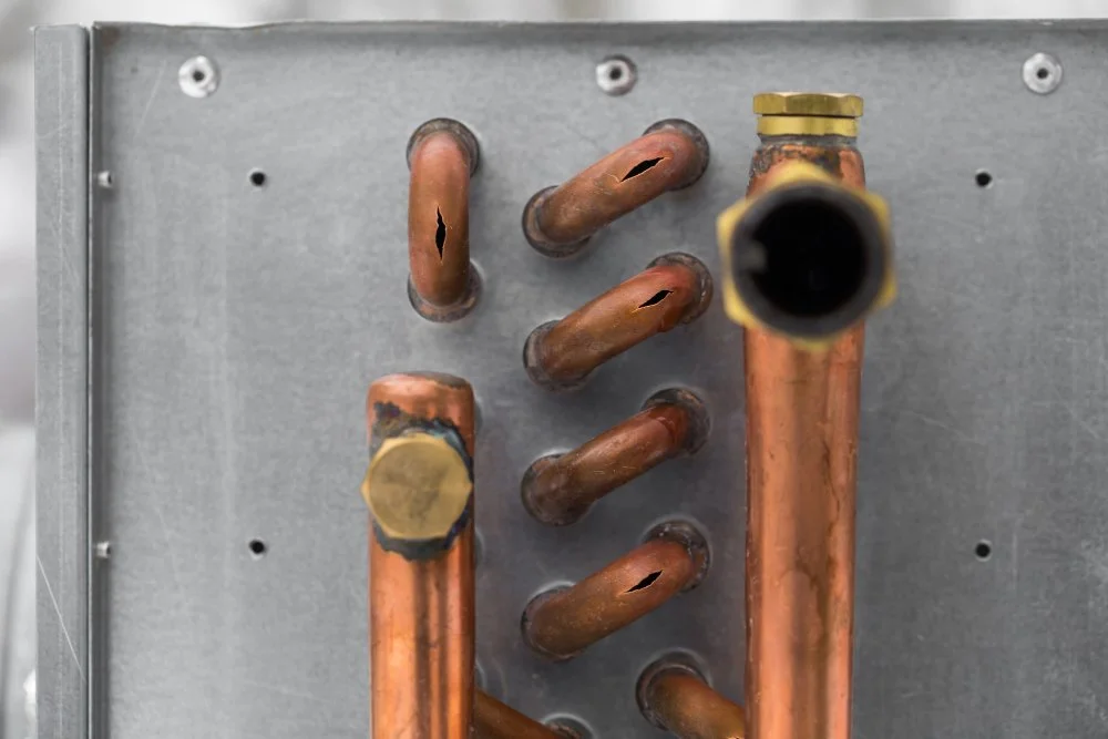 Close-up of a metal panel with multiple bent copper pipes, some with blackened and damaged areas.