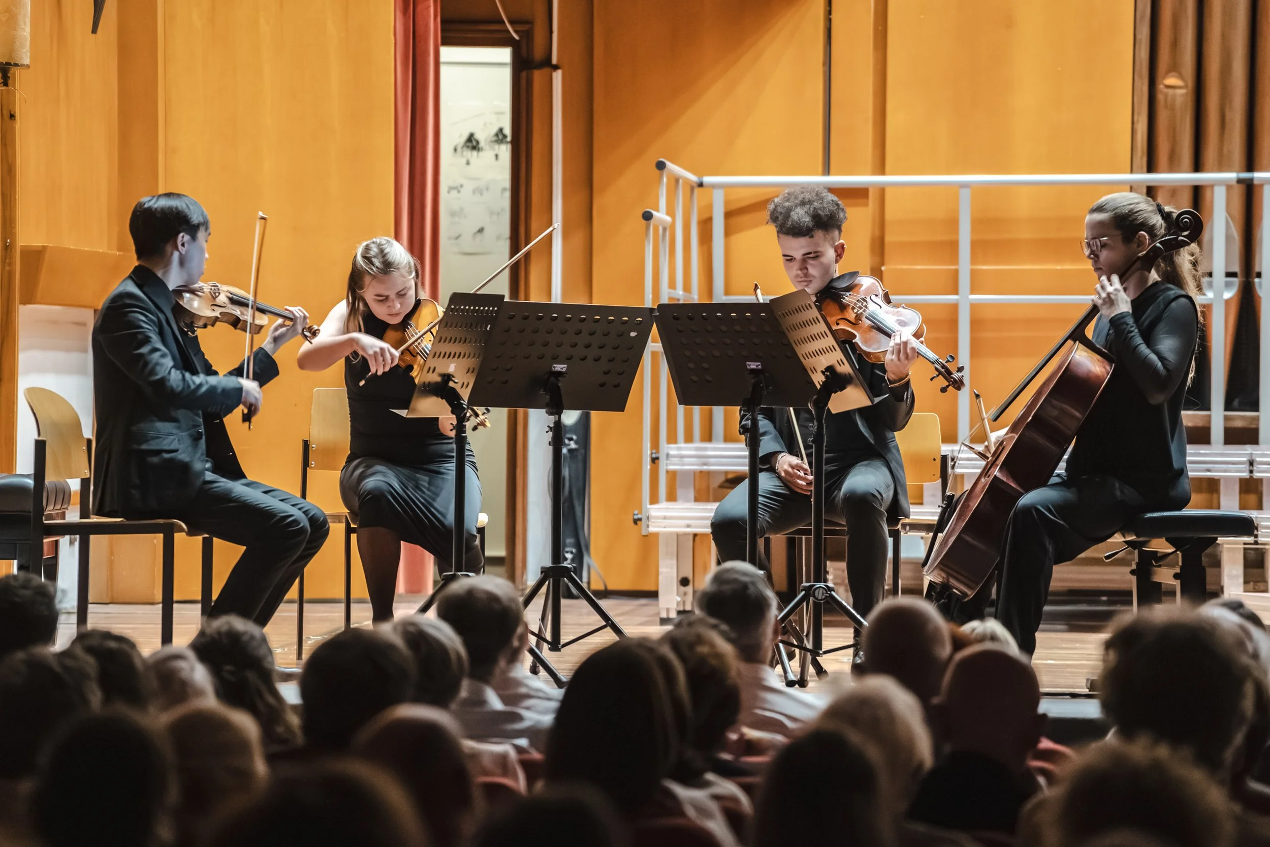 Four muscians playing a string quartet during a concert on stage, with an audience watching.