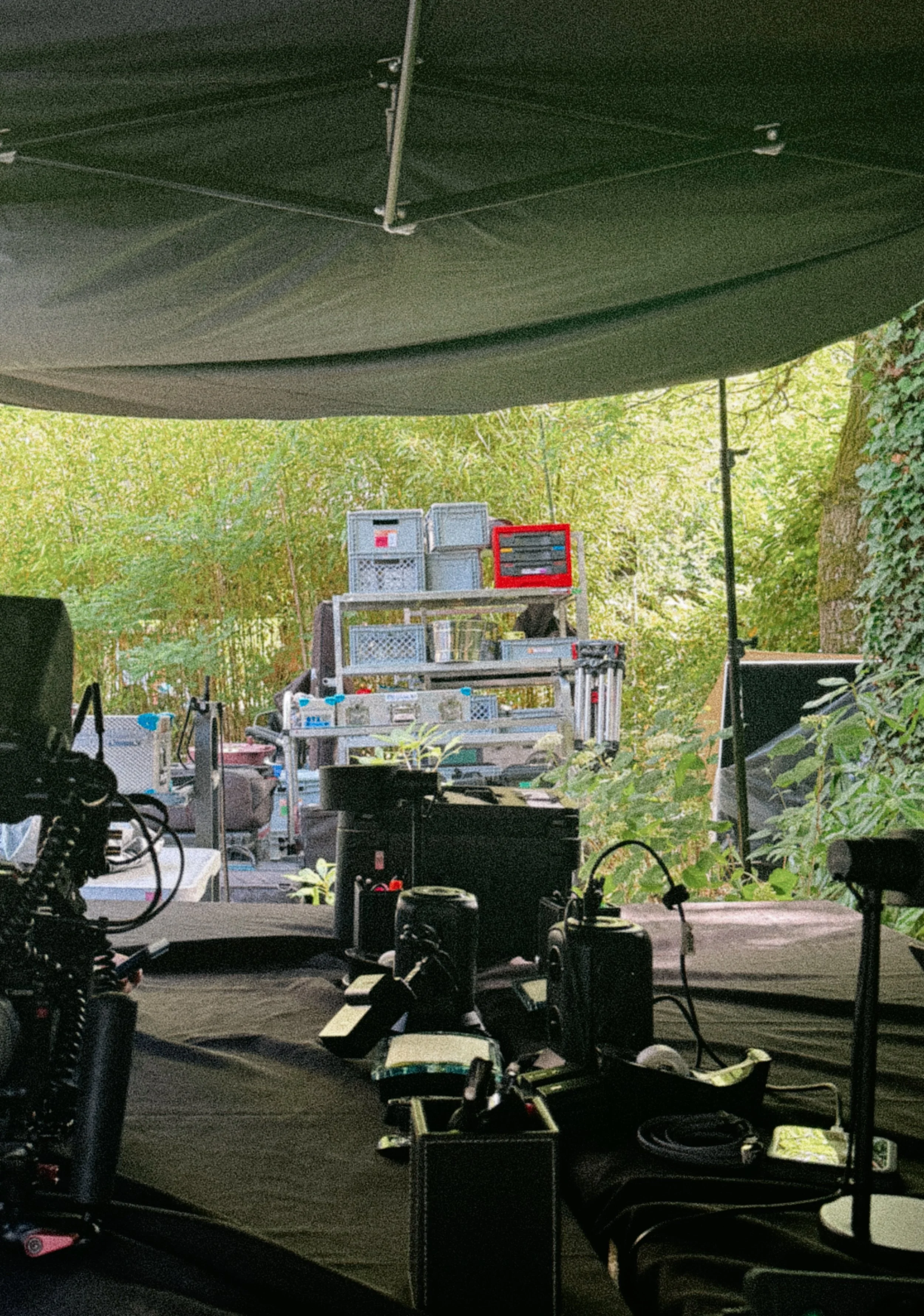 A photography studio with equipment, including cameras, lighting, and tables, set up for a shoot in an outdoor green space with trees and bushes in the background.