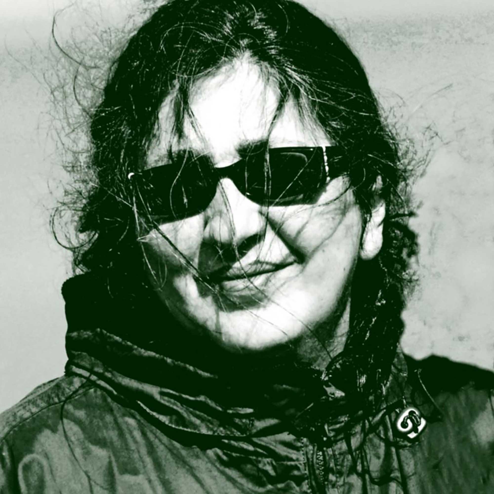 A black and white abstract image featuring a person's face with long, messy hair covering parts of the face and wearing sunglasses, with a distorted and artistic style.