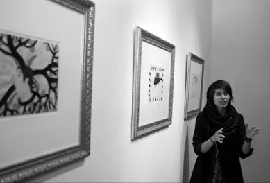 A woman standing in an art gallery with three framed artworks on the wall.