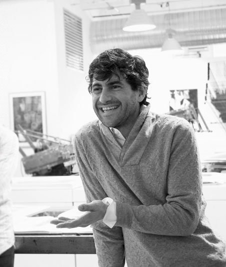 A man smiling and gesturing with his hand in a workspace or office.