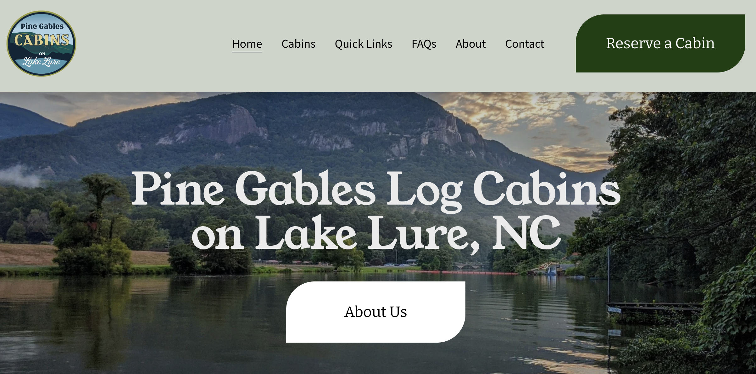 Website homepage header for Pine Gables Log Cabins on Lake Lure, NC, featuring a scenic view of a mountain and a lake at sunset.