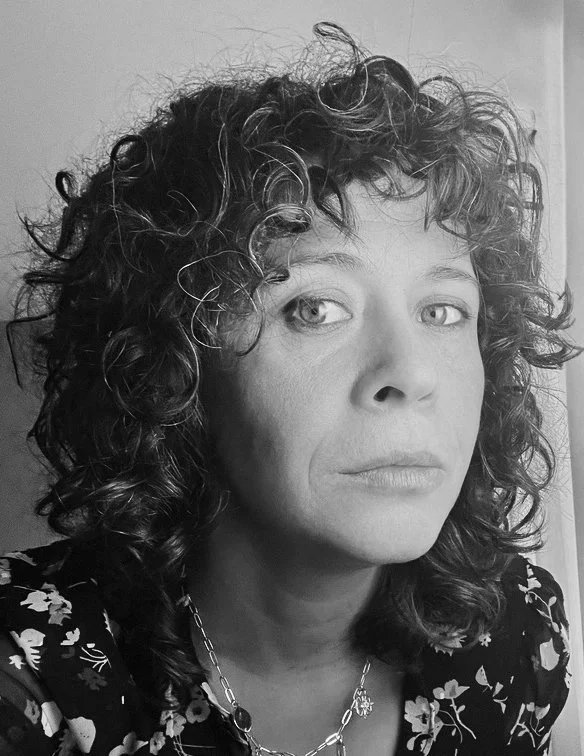 Black and white photo of a woman with curly hair, wearing a floral patterned top and a necklace.