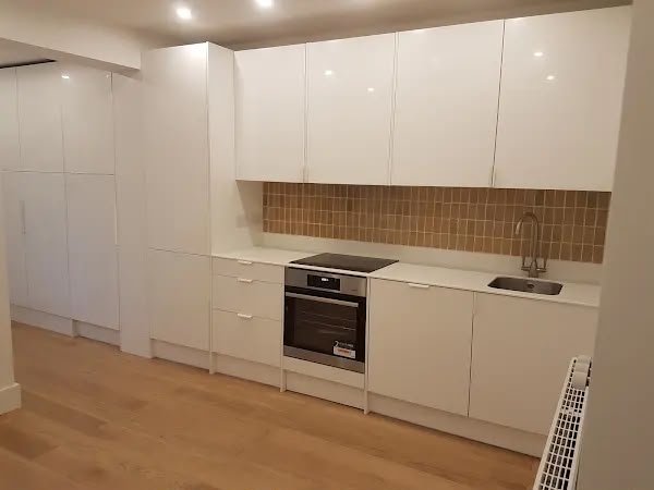 Modern kitchen with white cabinets, built-in oven, electric stovetop, sink, brown tiled backsplash, and wooden flooring.