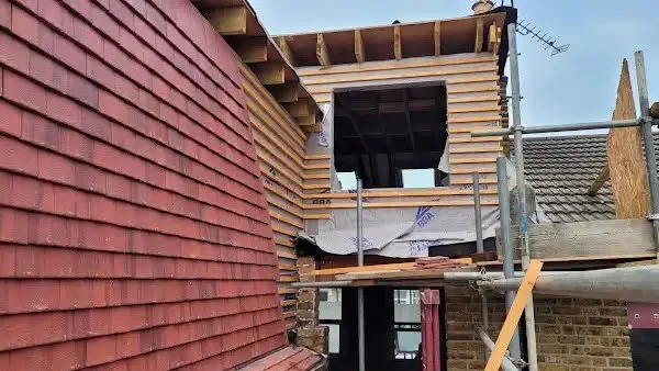 Construction site with brick and wood framing, scaffolding, and an opening for a window or door.