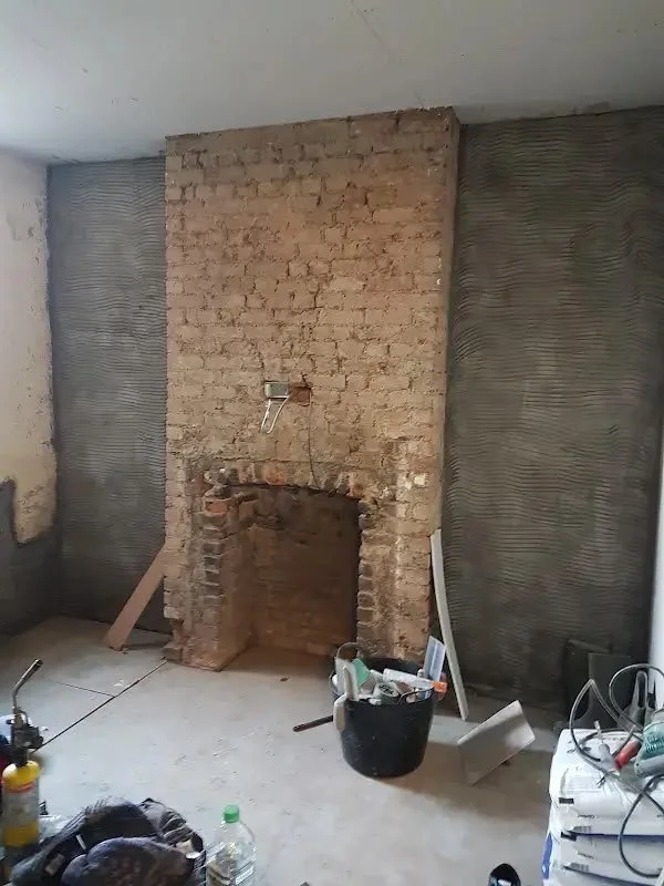 Unfinished room under renovation with exposed brick fireplace, construction tools, and building materials scattered around.