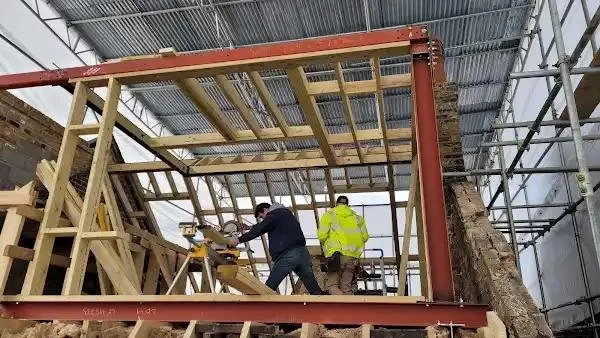Construction workers building a wooden structure inside a metal framework, with scaffolding surrounding the area.