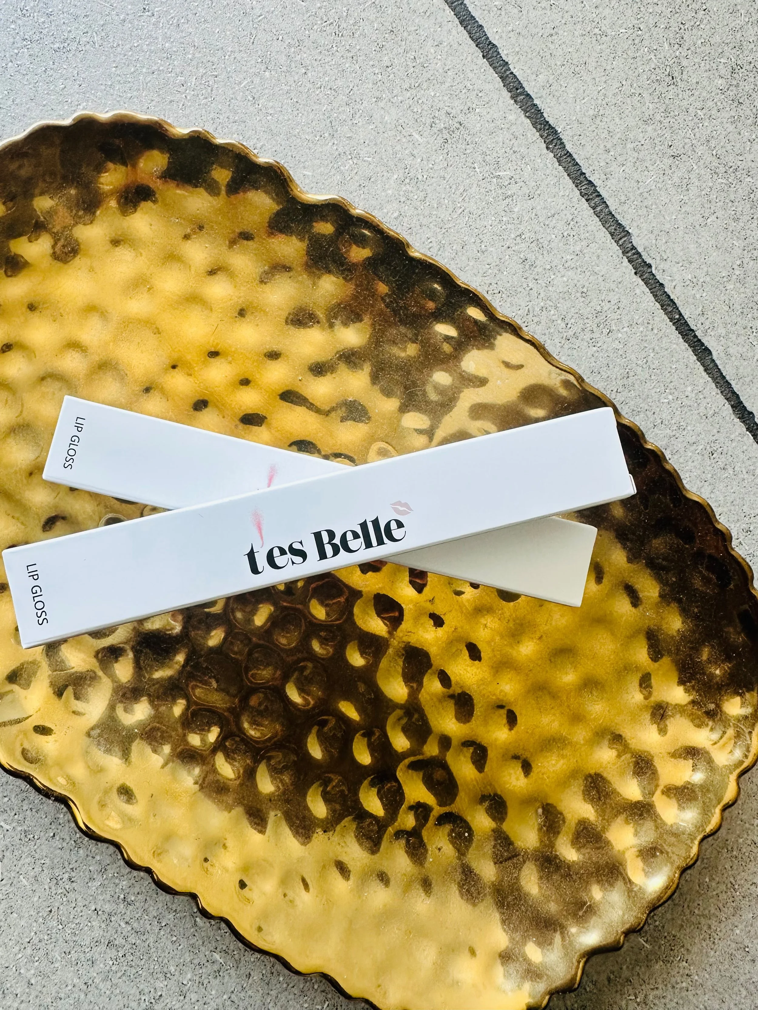 A decorative gold-colored dish with black spots, resembling a honeycomb pattern. Part of a white box labeled 'tés Belle' is visible on the dish.