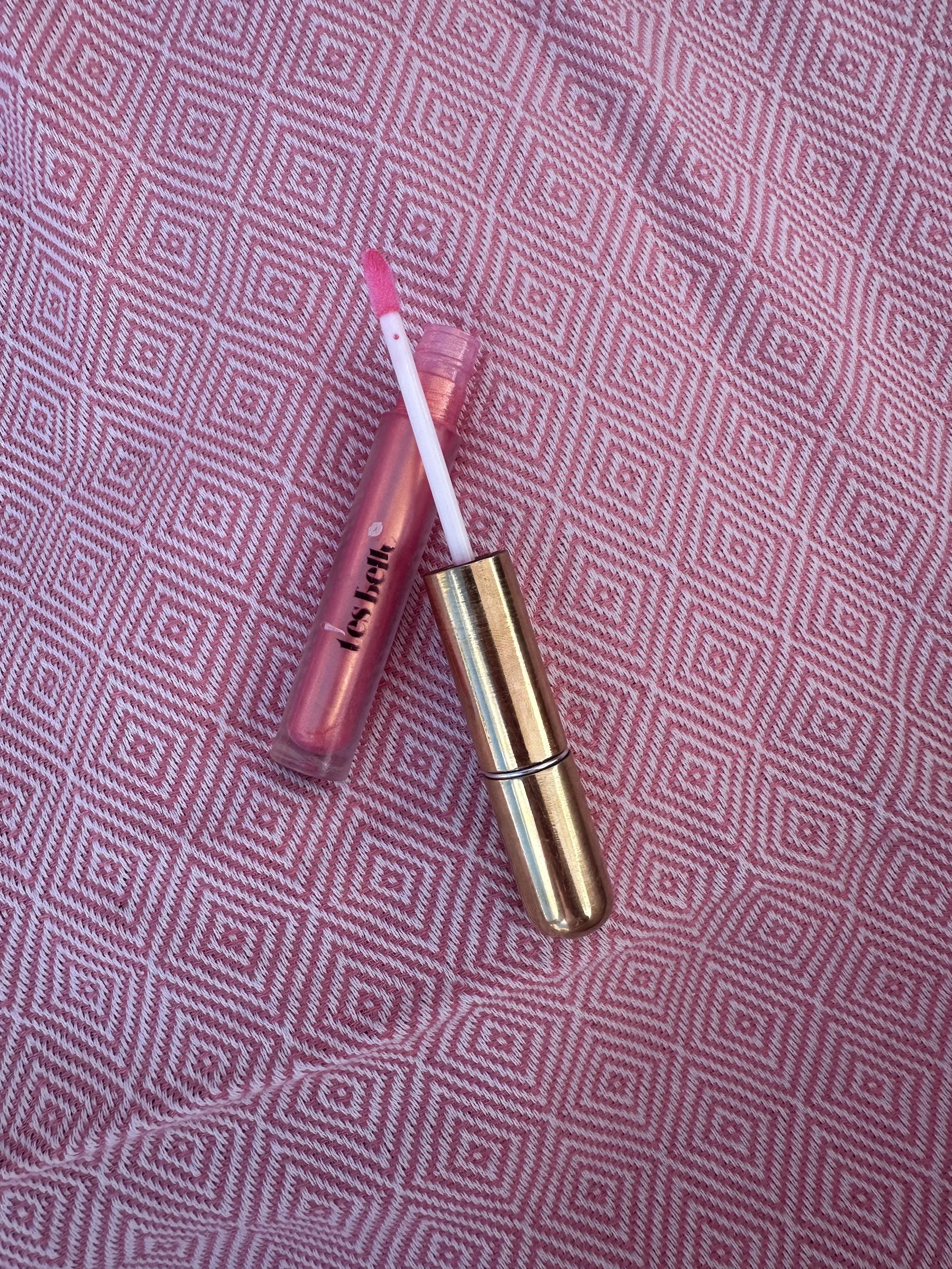 A close-up of a metallic spray bottle with a black spray nozzle on a pink fabric with a geometric diamond pattern.