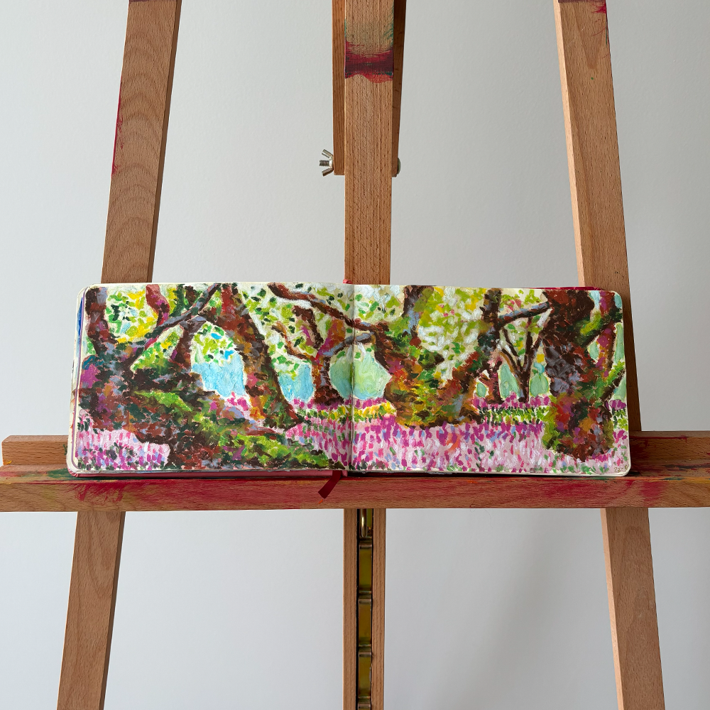 Livro aberto com uma pintura de um cenário natural de árvores e um campo de flores, apoiado em uma escada de madeira.