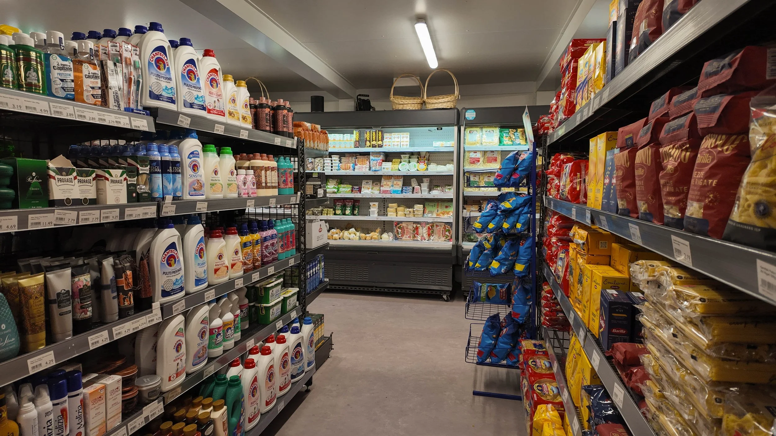 Supermarktregale mit Reinigungsprodukten, Käse und Snacks, Kühlregal im Hintergrund.
