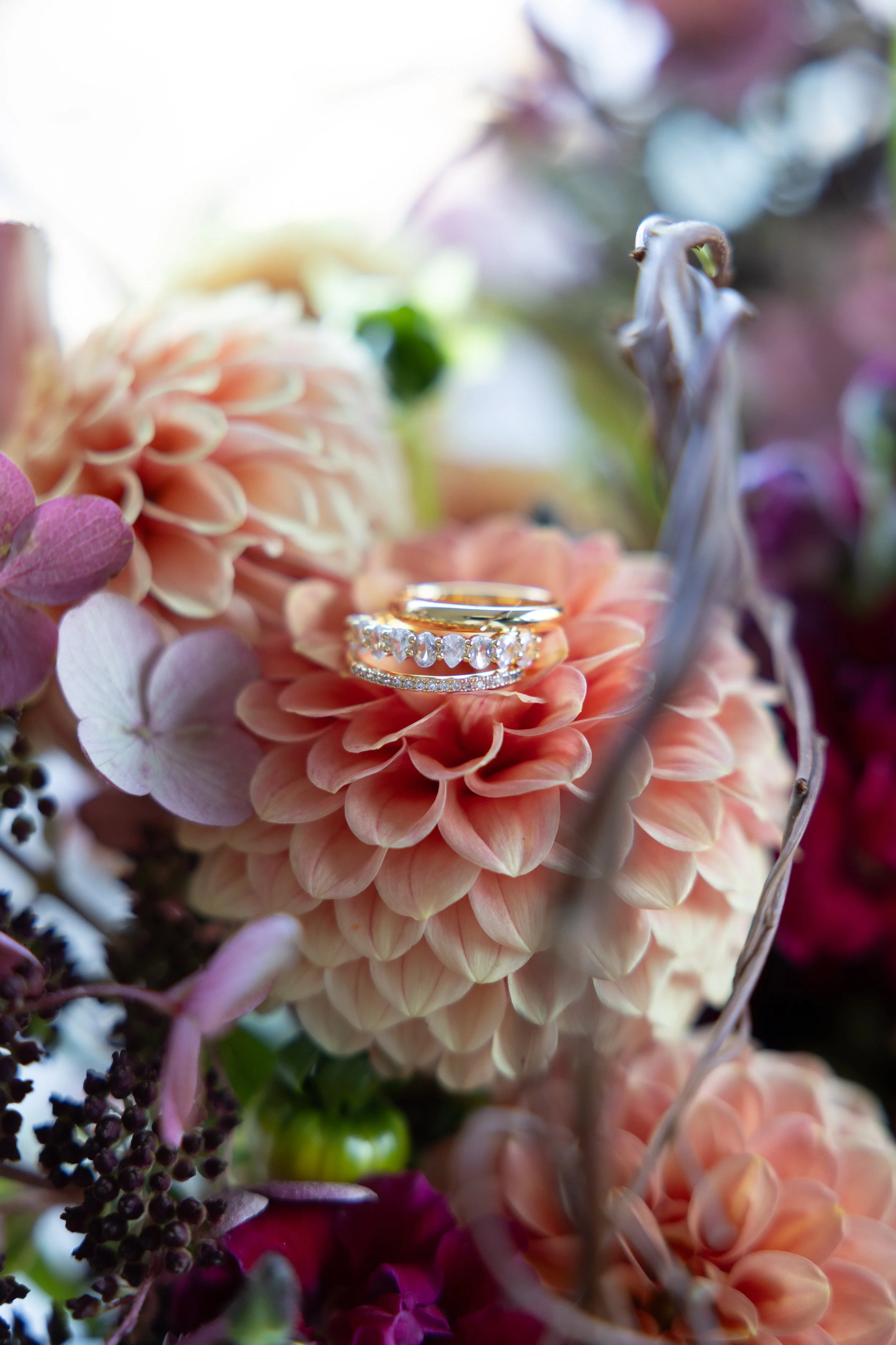 Close-up of a bouquet of pink and purple flowers with wedding rings resting on a peach-colored flower.