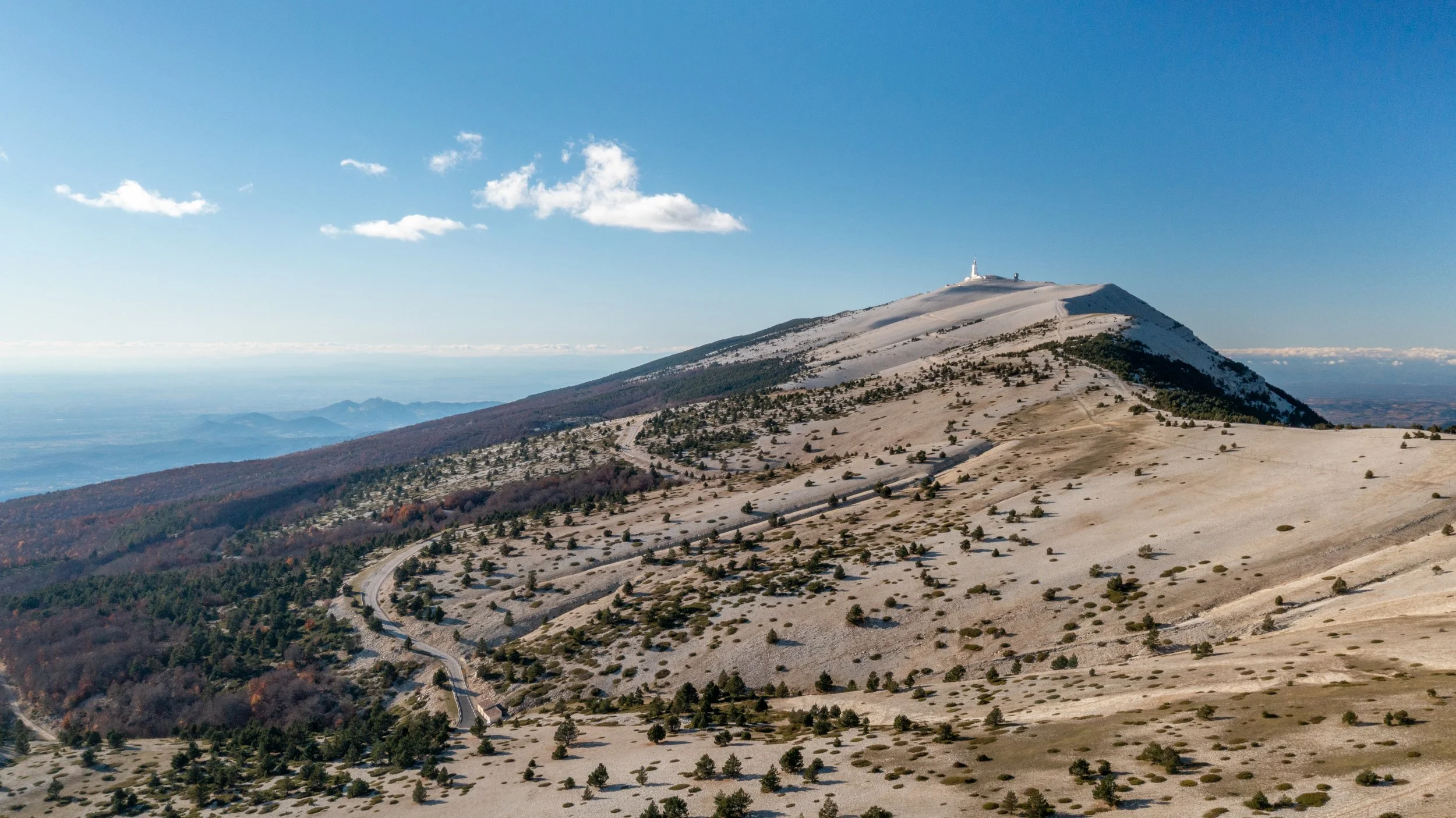 Montagne avec sommet enneigé et vue sur la vallée en dessous, ciel bleu avec quelques nuages.