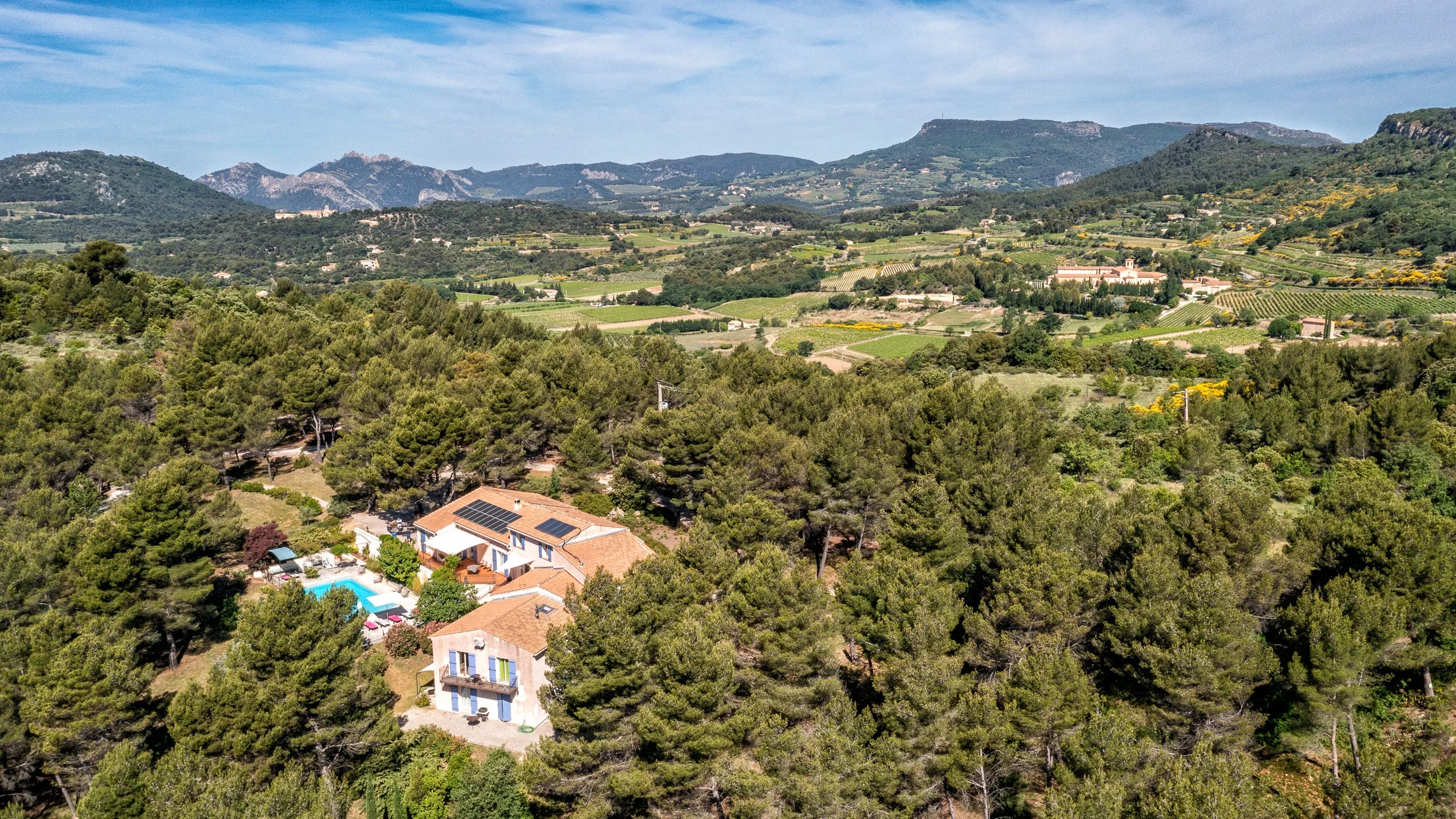 Paysage rural avec montagnes, champs agricoles, et maisons entourées d'arbres.