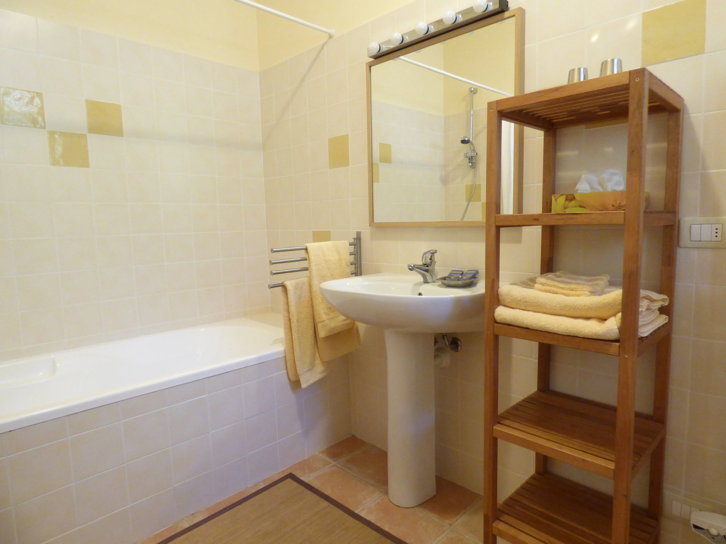 Interieur d'une salle de bain avec une baignoire, un miroir, un lavabo, une étagère en bois avec des serviettes, et un sèche-serviettes adapté pour suspendre des serviettes ou des vêtements.