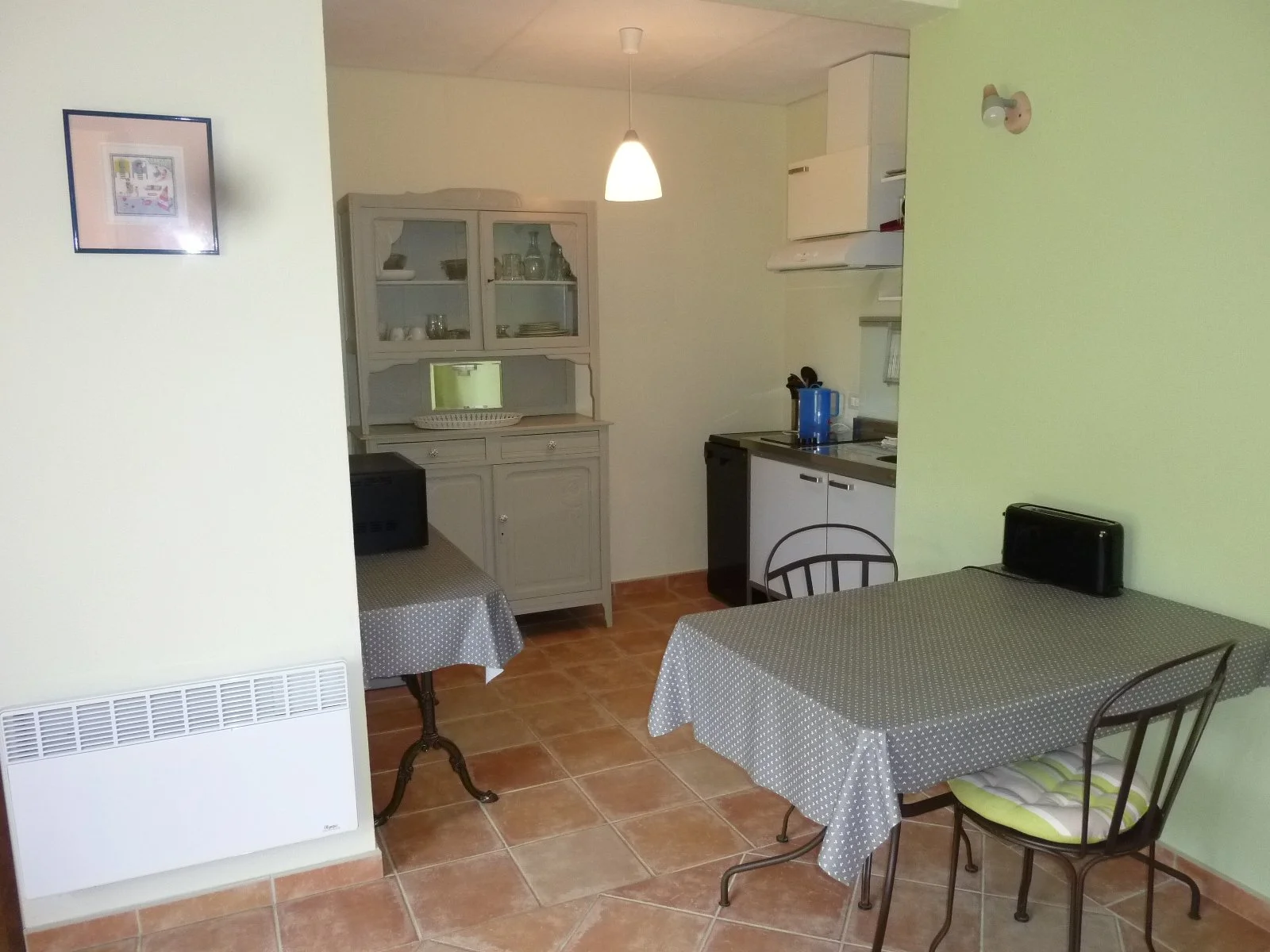 Cuisine avec deux tables, une équipée de chaises, cheminée, vaisselier blanc, placard de cuisine, et murs peints en vert et blanc.