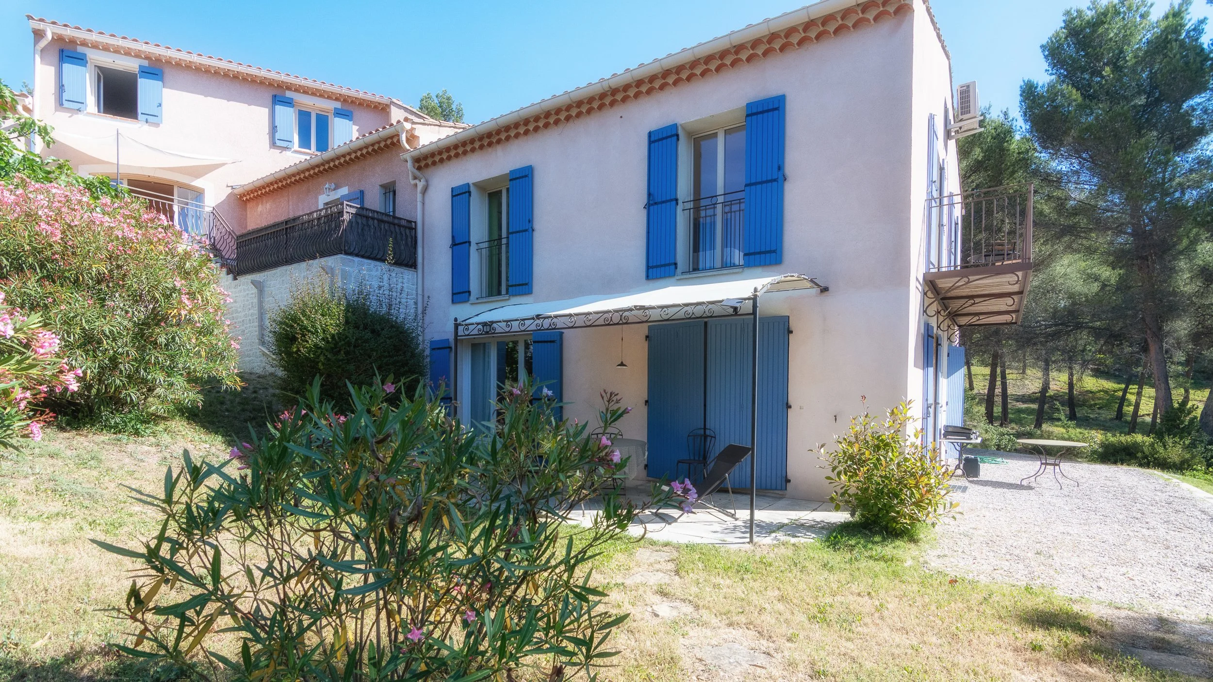 Villa avec fenêtre à volets bleus, balcon, et Jardin avec arbres et fleurs.