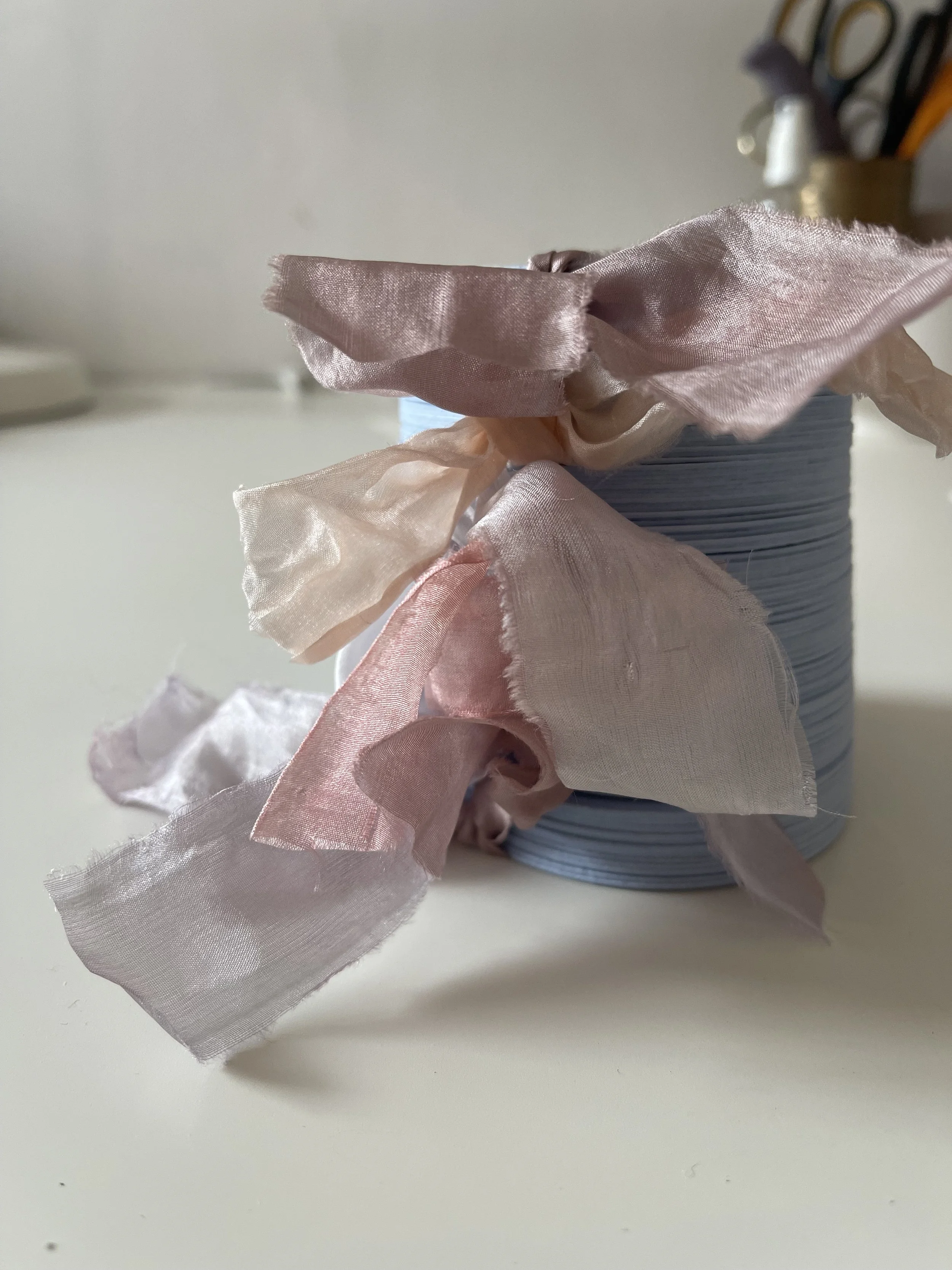 A roll of light pink and gray striped ribbon with frayed edges on a white surface, partially unrolled with some ribbon hanging off the side.