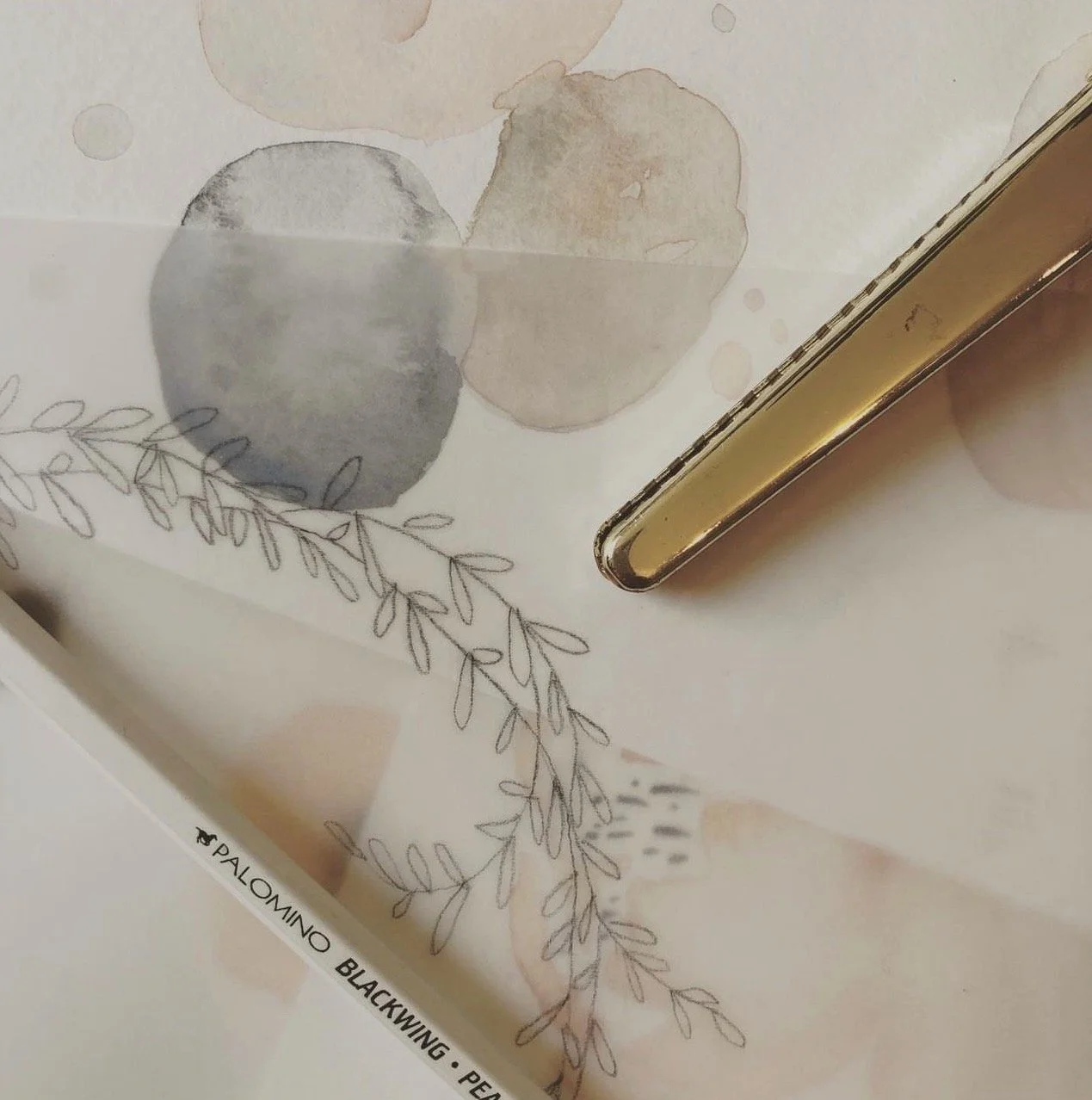 Close-up of a piece of paper with watercolor circles and leaf drawings, with part of a gold-colored metallic object visible on the right side.