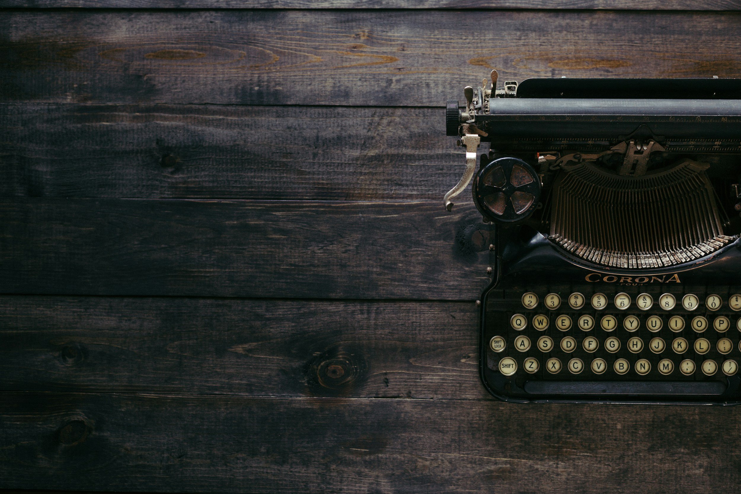 An antique black typewriter with cream-colored keys on a dark wooden surface.