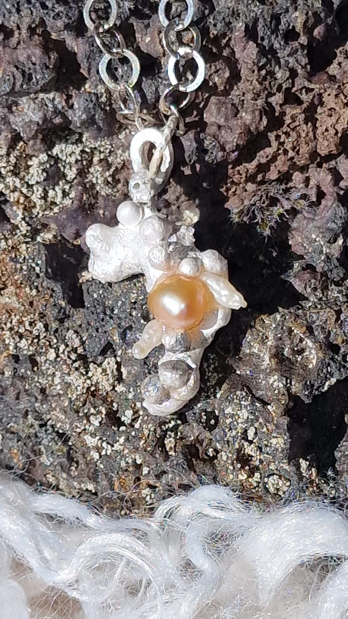 A necklace with a pendant resembling a bear, located on a rocky surface surrounded by fluffy white material.