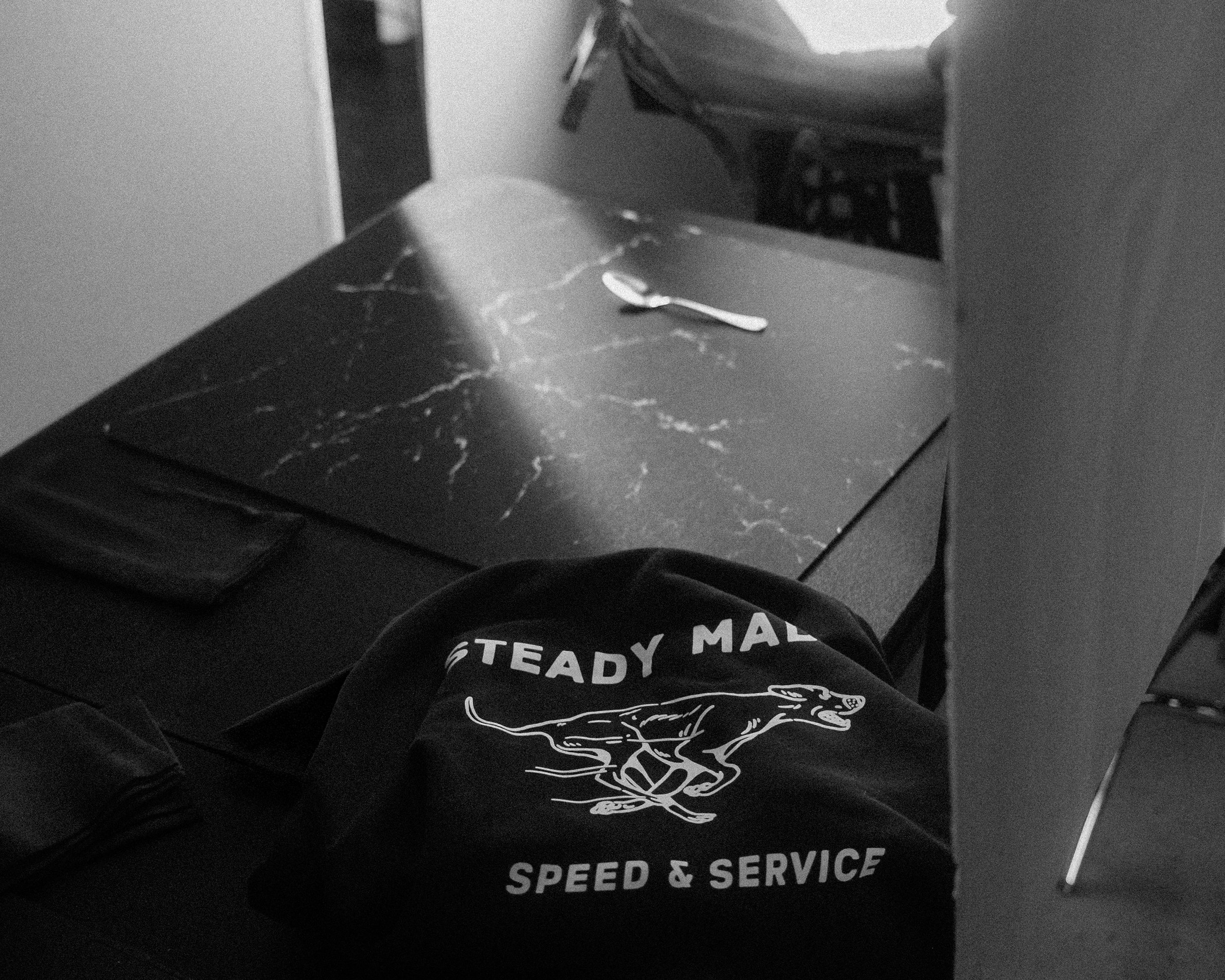 A person wearing black pants with a graphic of a dog and text that reads 'Speed & Service' in white, sitting or lying on dark furniture with a marble top, with a spoon on the table.