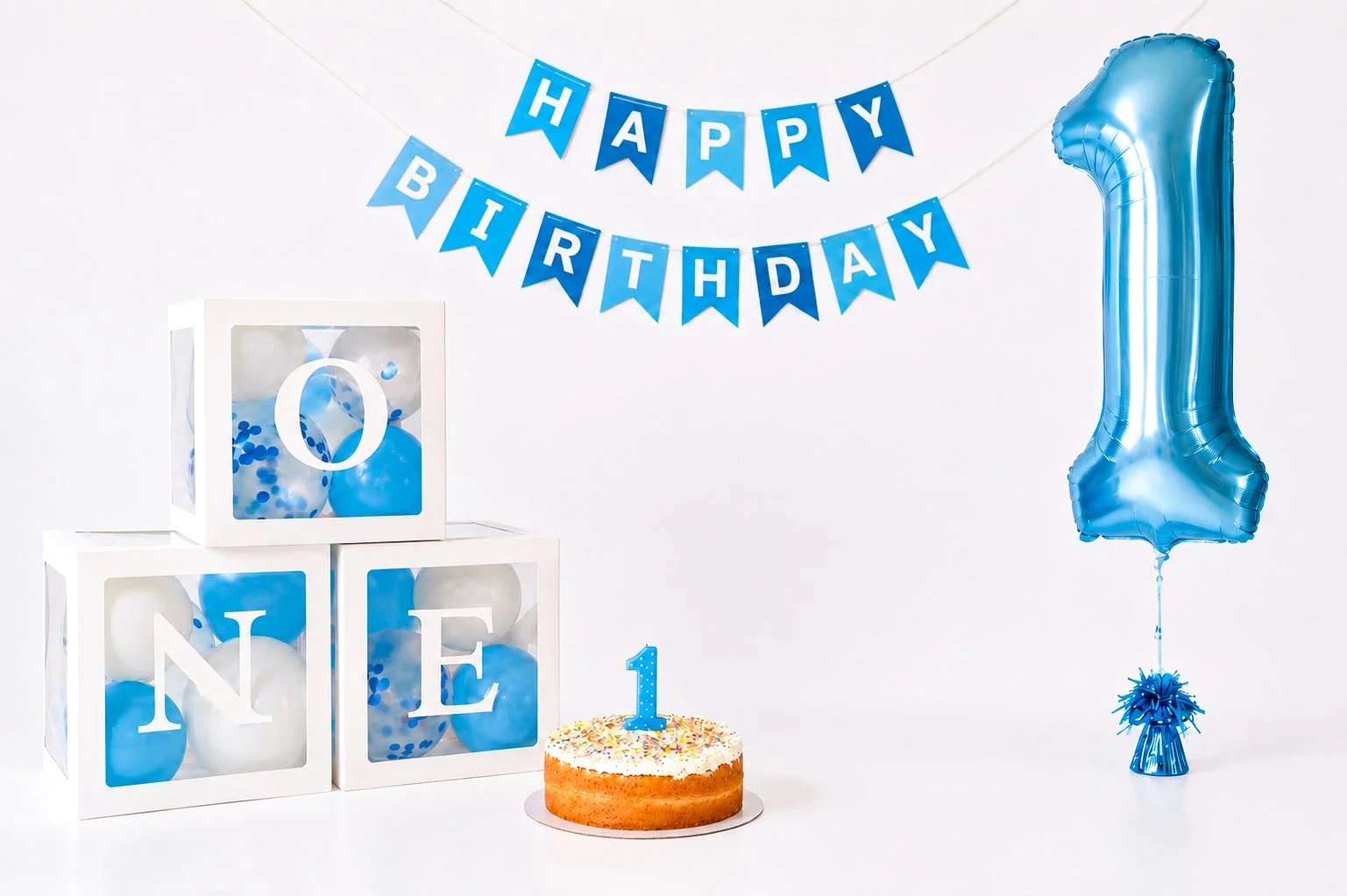 Decorations for a first birthday party include a blue balloon in the shape of the number one, a cake with a blue number one candle and sprinkles, a banner that reads 'HAPPY BIRTHDAY,' blue and white balloons in transparent boxes, and a large blue num