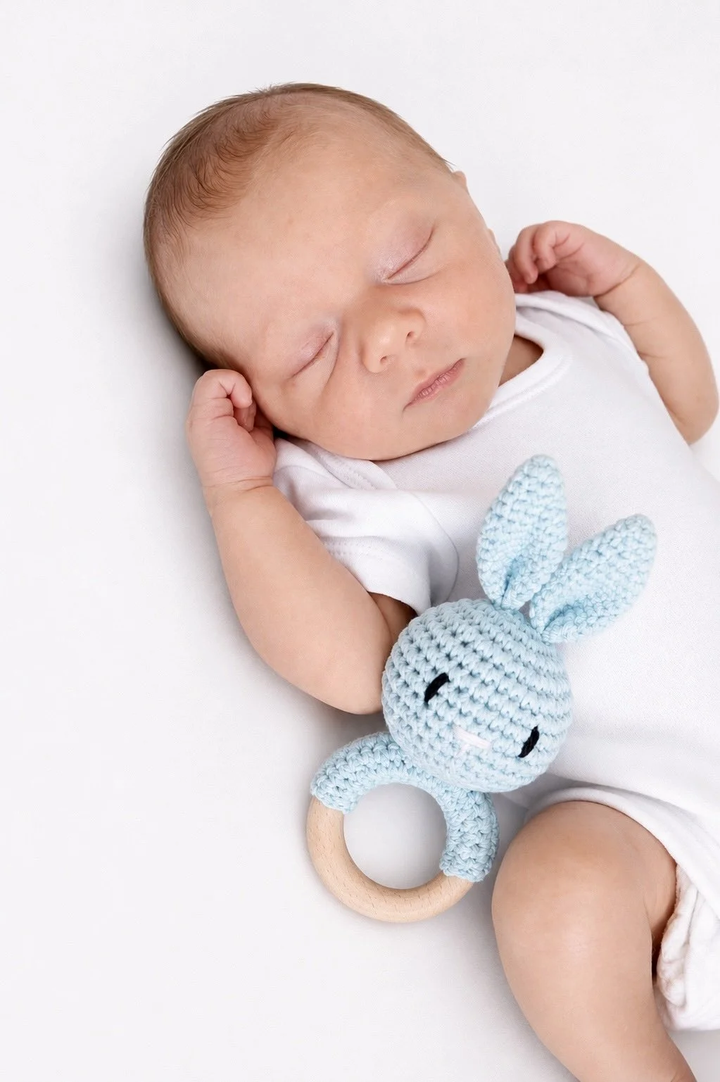 A sleeping baby with a crocheted blue rabbit teething toy.