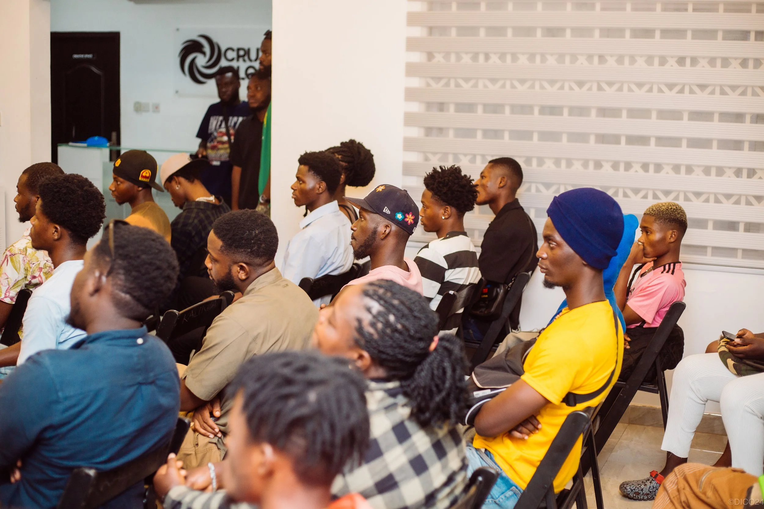 Group of diverse young adults seated, attending a presentation or event in a modern indoor space.