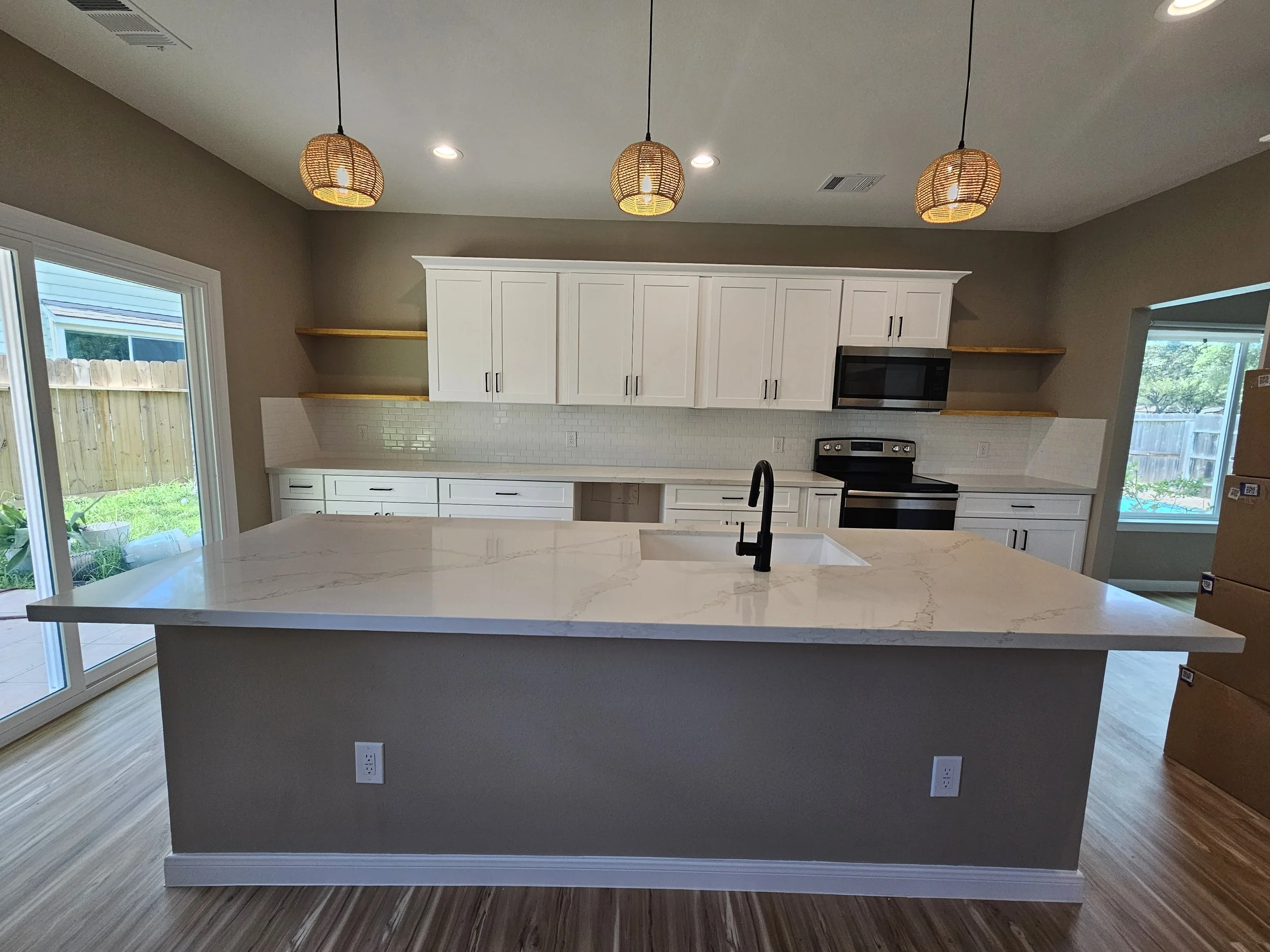 Modern kitchen with white cabinets, a marble island, pendant lights, and sliding glass doors overlooking a backyard.