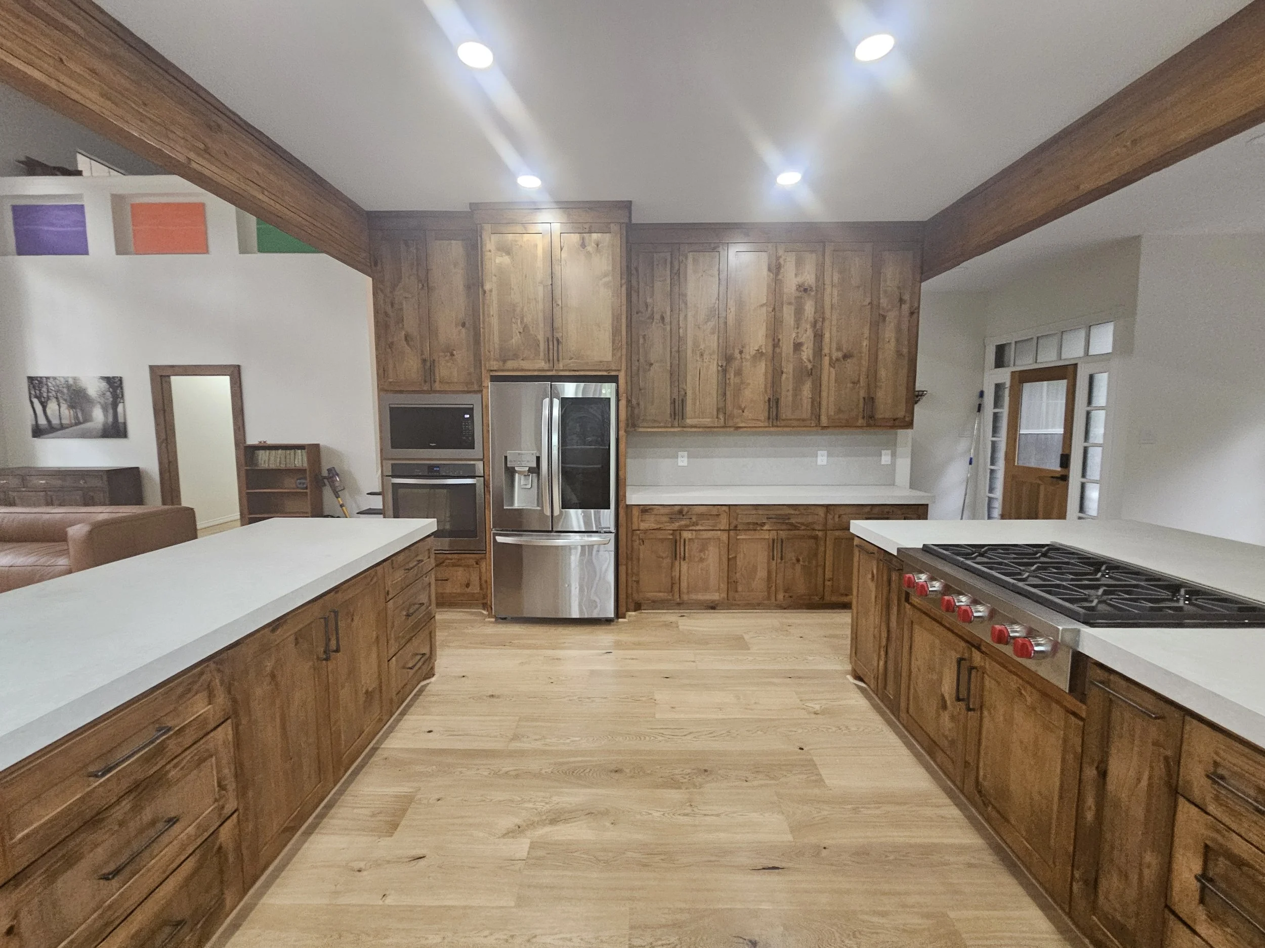 Kitchen remodeling with wooden cabinets, white countertops, stainless steel appliances, and hardwood flooring. Recessed lighting in the ceiling and French doors leading outside.