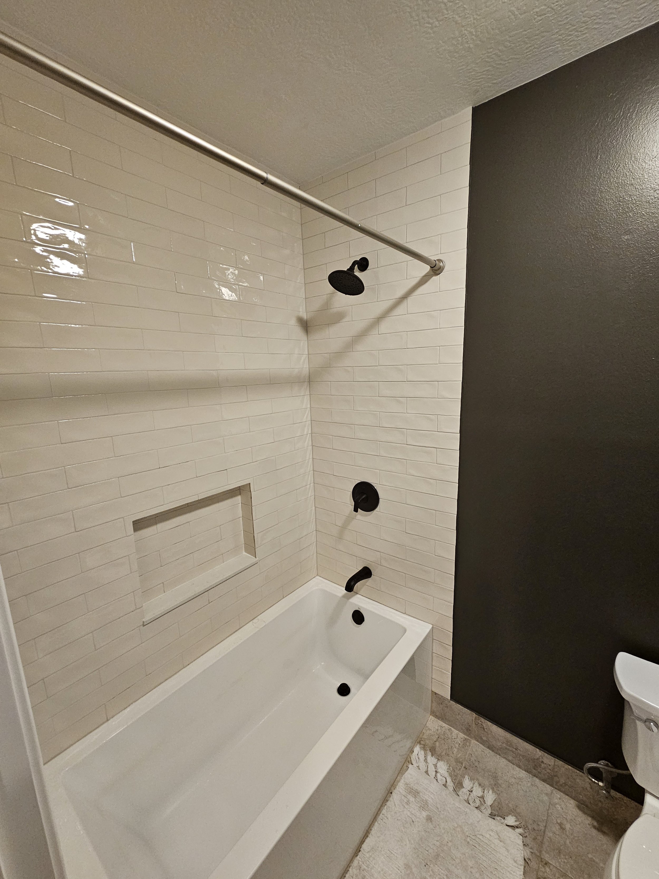 Bathroom shower area with white subway tile walls, a black showerhead, a bathtub, and a gray wall on the right side.