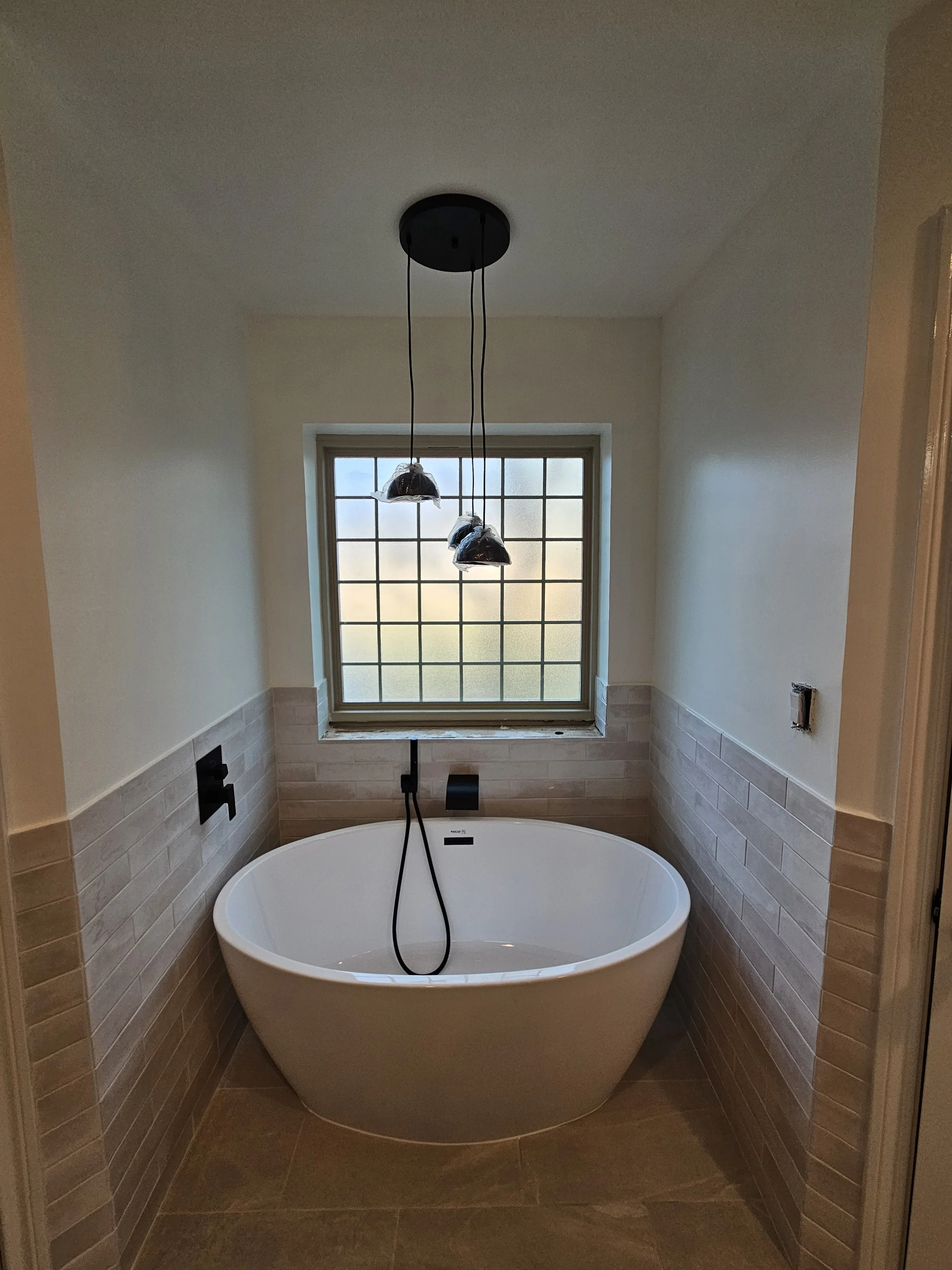 Bathroom with a freestanding oval bathtub, large window with grid pattern, and a modern black pendant light fixture with three hanging lamps.