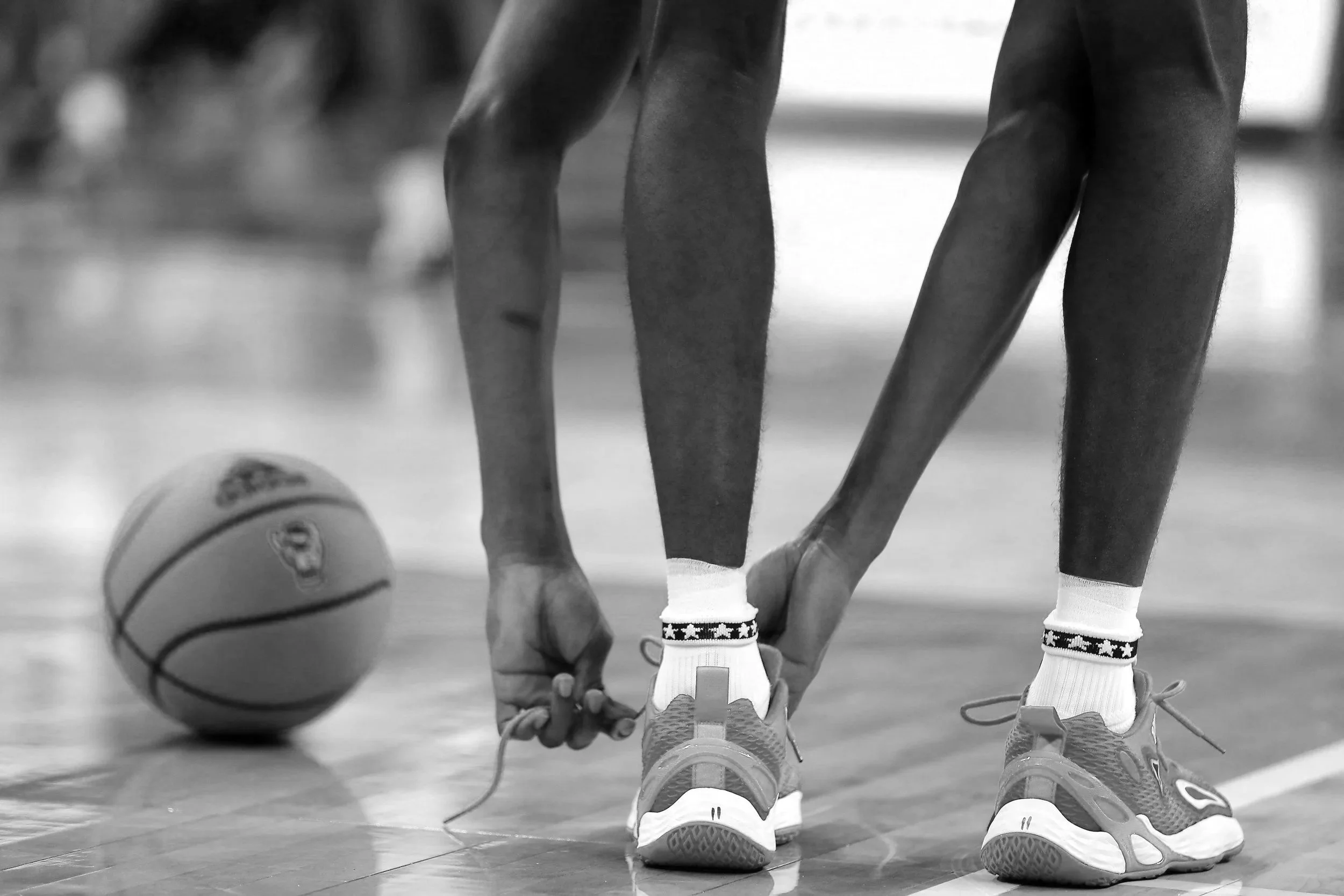 An athlete tying sneakers with striped socks, and a basketball nearby.