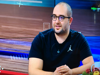 Simeon Marinov sitting at a table in a sports studio, with a basketball court in the background.