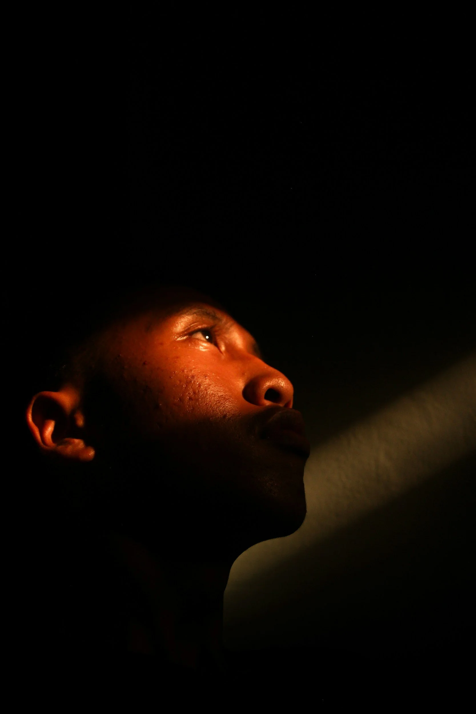 Close-up of a person's face, illuminated from below, with dark background, showing their eye, nose, and mouth.