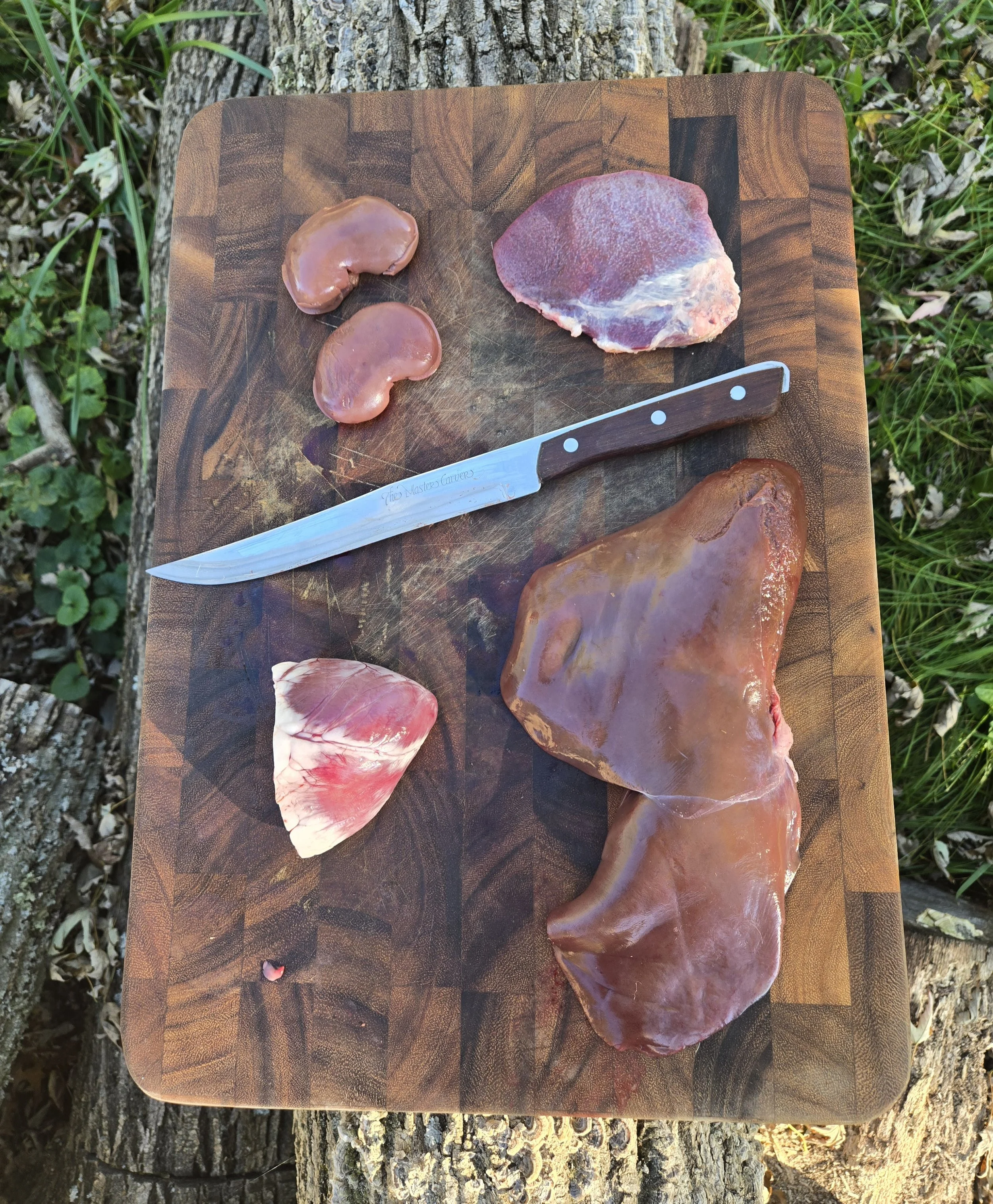 Pork liver, heart, kidneys, and spleen arranged on a wooden cutting board with a butcher knife.
