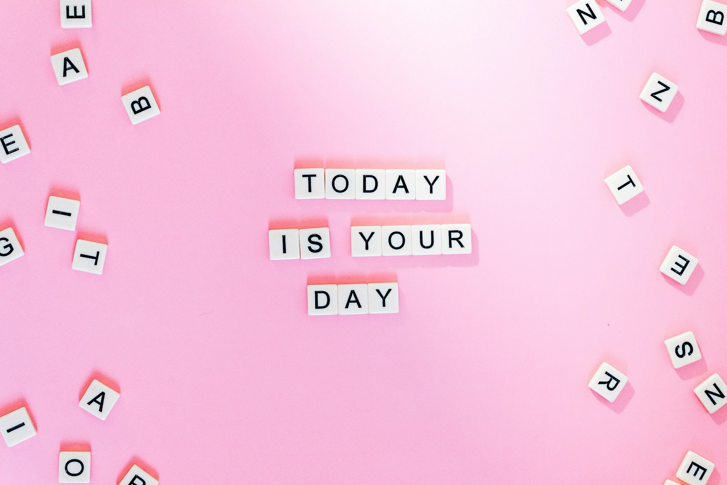 Pink background with letter tiles spelling out 'TODAY IS YOUR DAY' arranged in the center, surrounded by scattered letter tiles.
