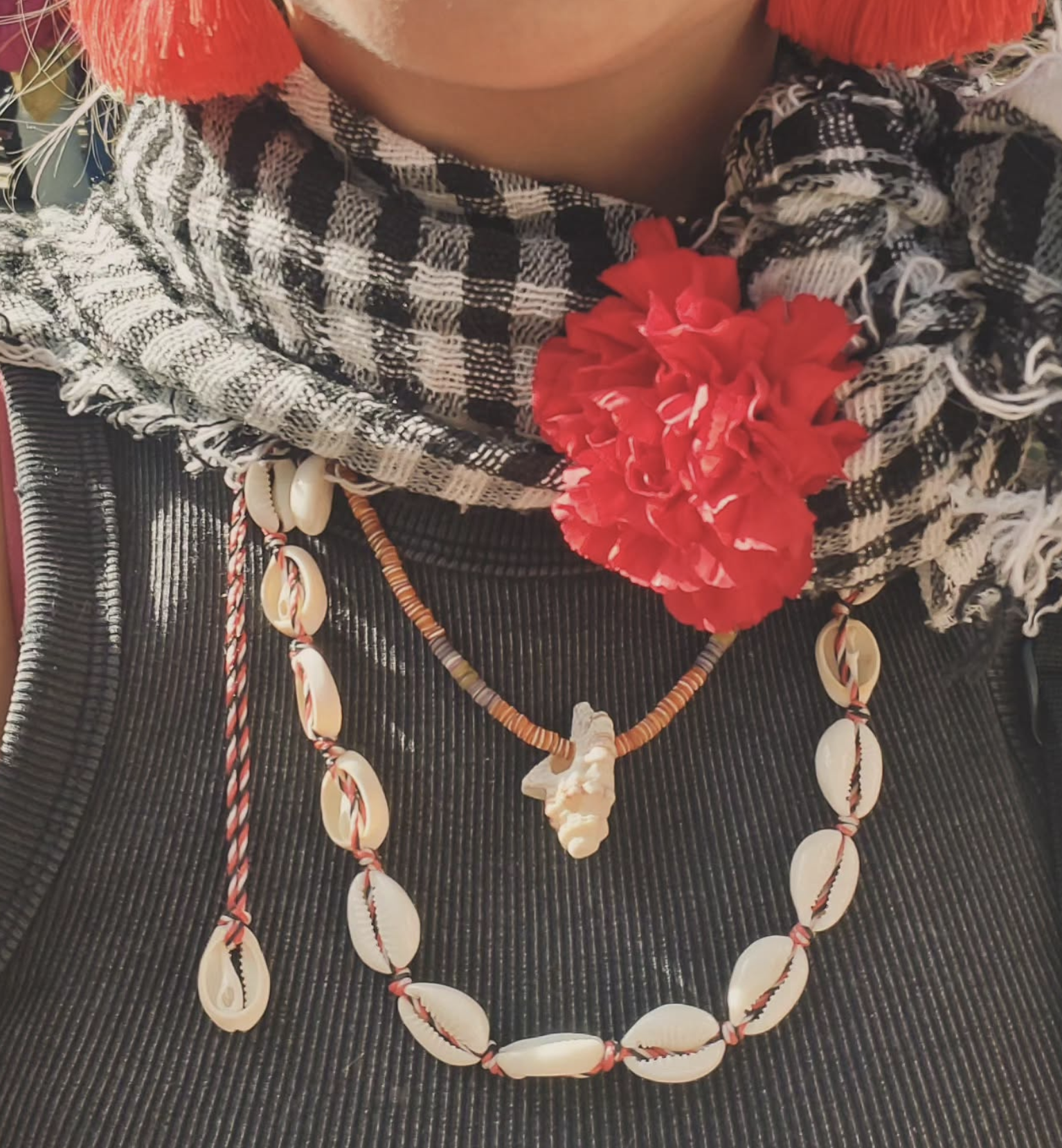 Close-up of a person wearing a checkered scarf, red flower accessory, shell necklaces, and traditional jewelry.