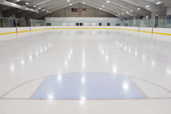 Empty indoor ice hockey rink with flags of the United States and Canada hanging above.