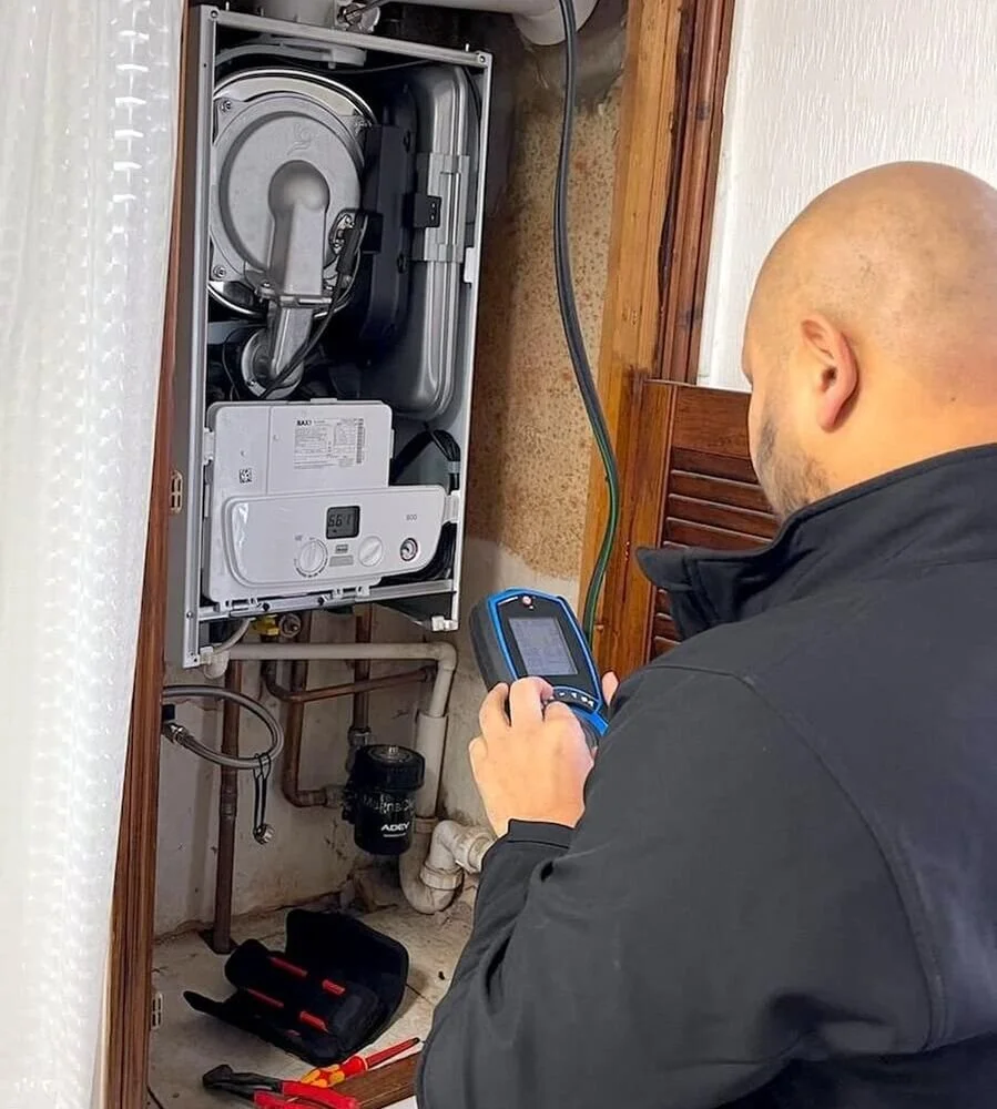 A technician inspecting or repairing a boiler using a handheld diagnostic device in a utility closet.