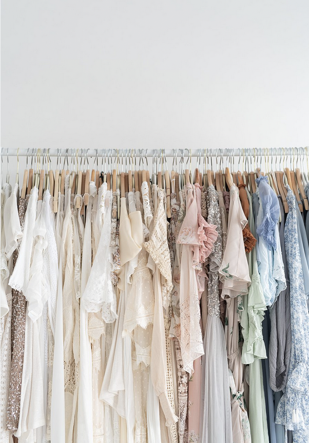 Clothes hanging on a rack organized by color, primarily in neutral, pastel, and cool tones.