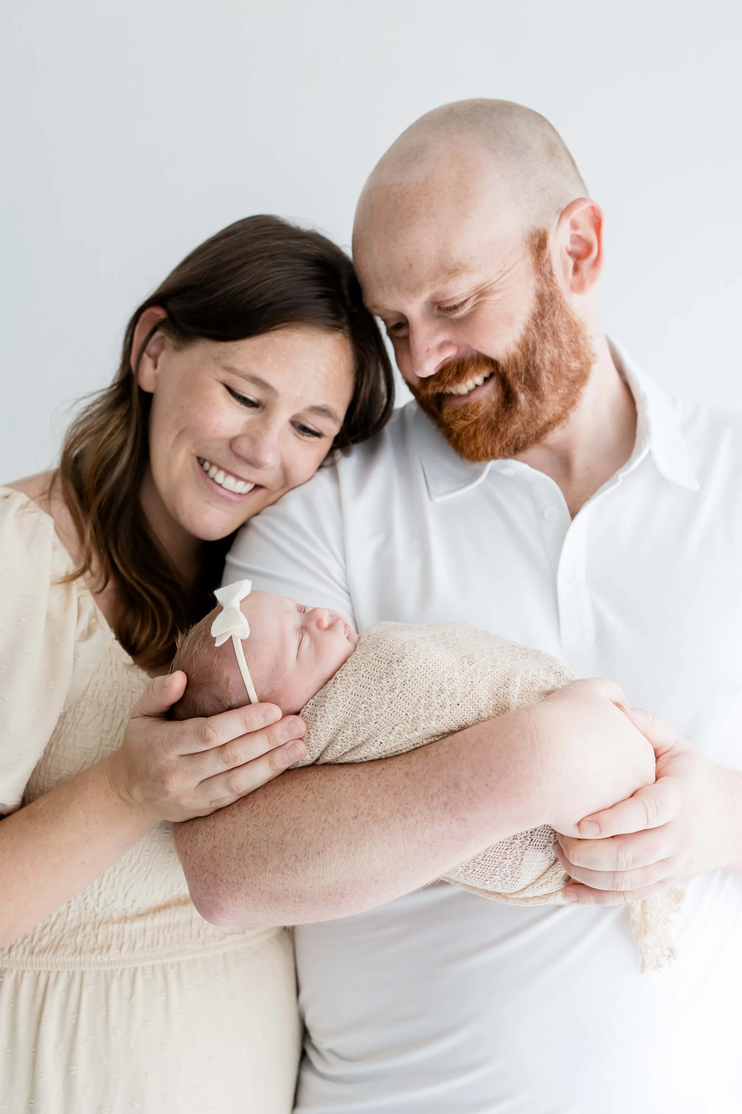 A couple holding a newborn baby, smiling and looking at the baby  at East and Elm Portrait Studio in Fairport, NY, during a newborn session.