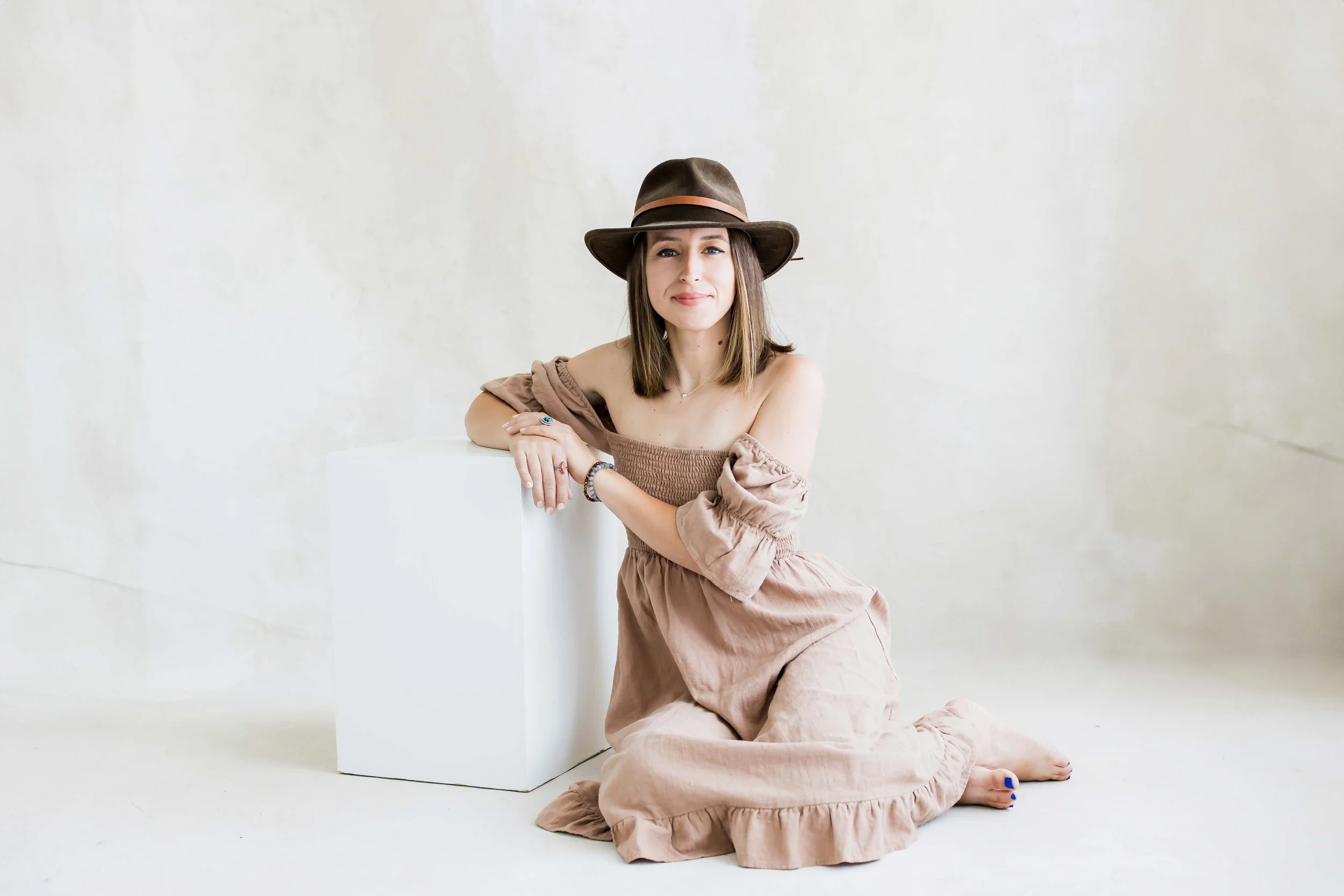 A woman sitting on the floor with her knees bent and arms resting on a white cube during branding and headshot photos with East and Elm Portrait Studio in Fairport, NY.