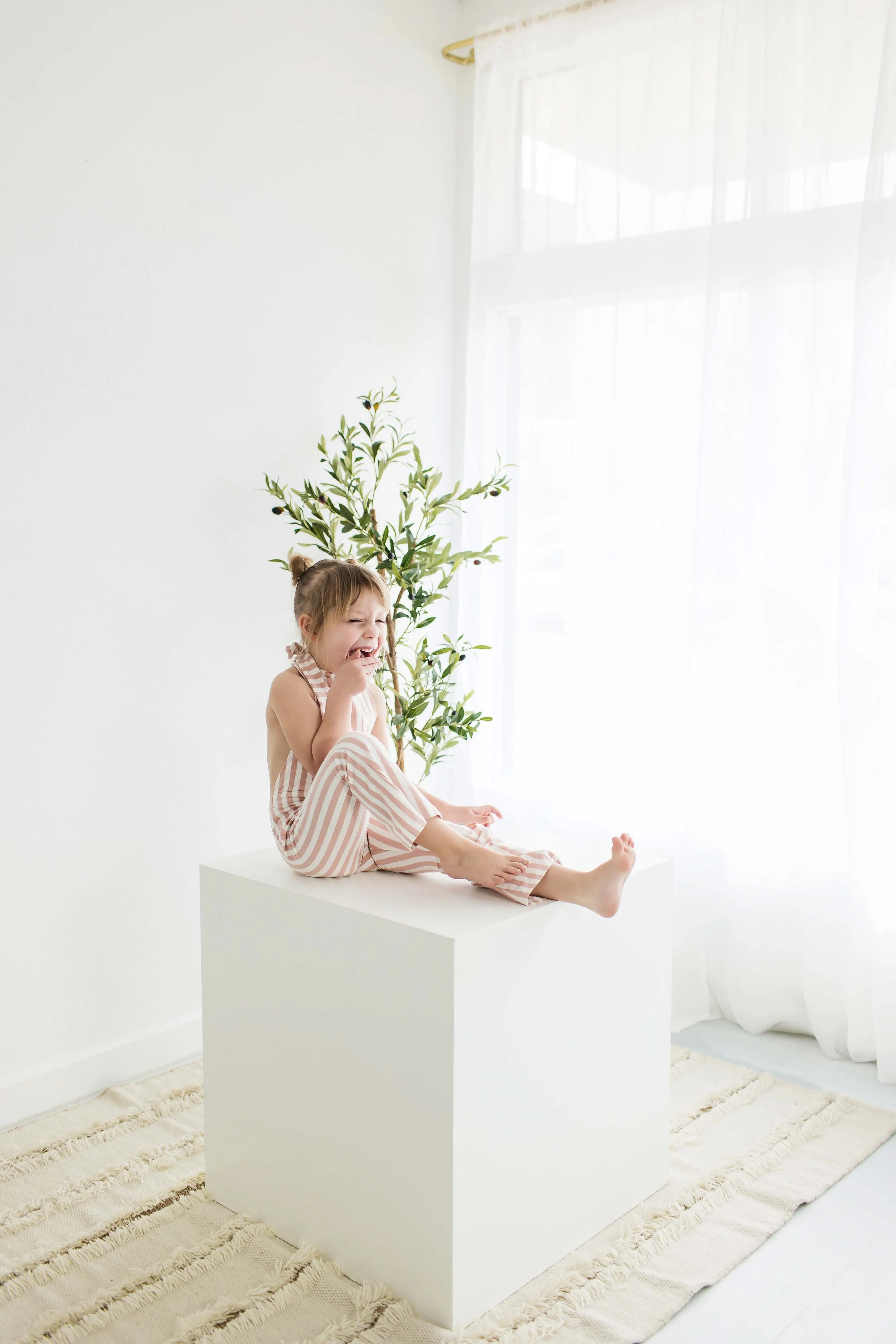 A young girl sitting on a white cube at East and Elm Portrait Studio in Fairport, NY, during a family photography session.